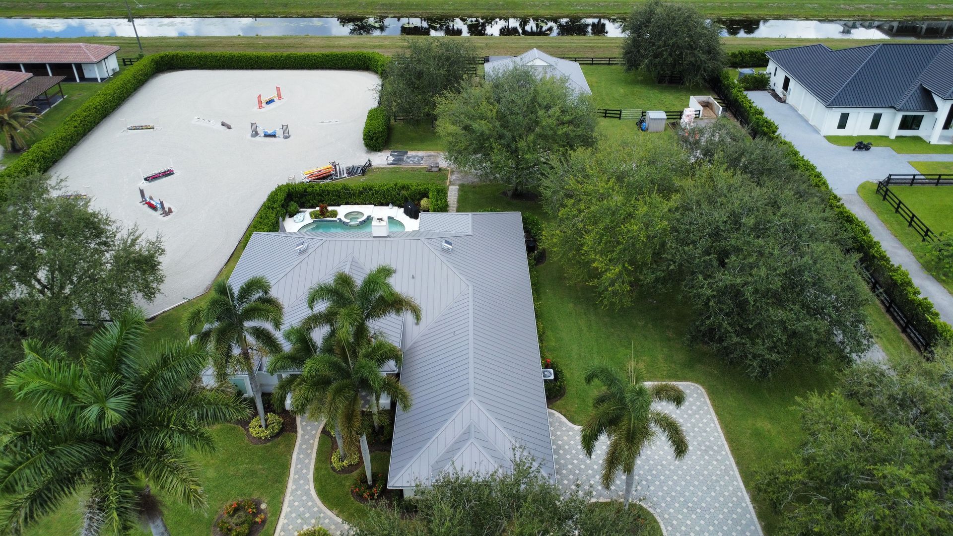 Aerial view of a white house with palm trees beside a lake and green lawns