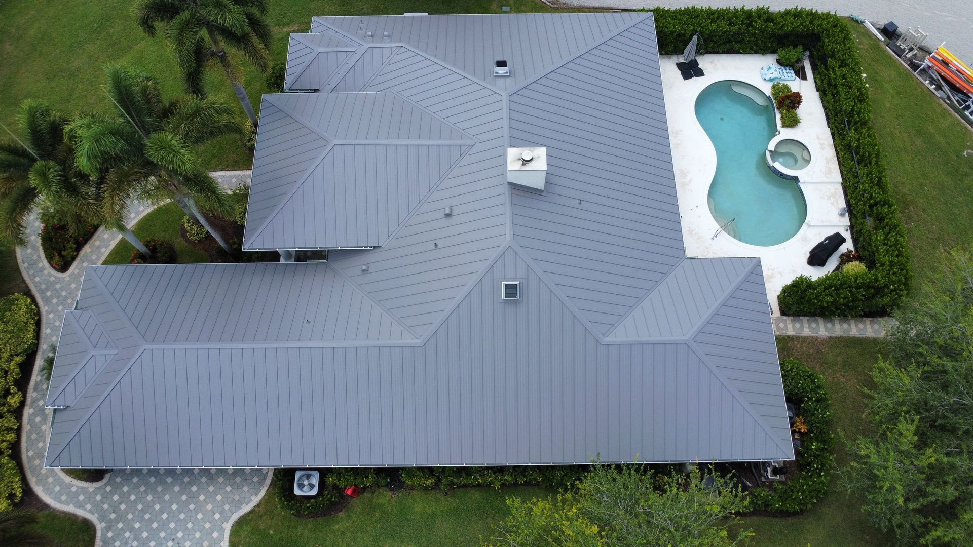 Aerial view of a gray-roofed house with a swimming pool and green yard
