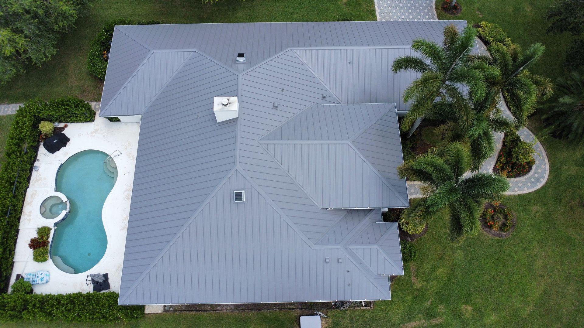 Aerial view of a gray-roofed house with a backyard pool and palm trees