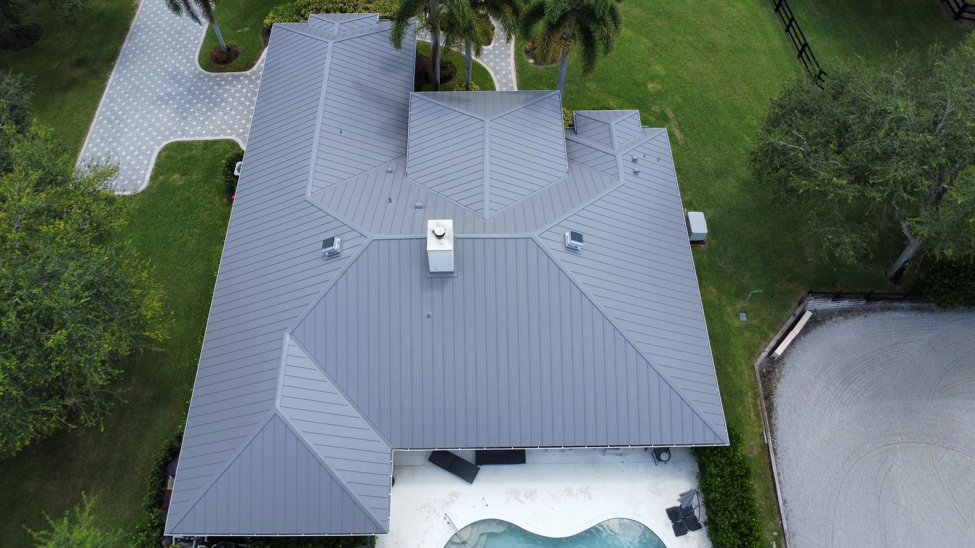 Aerial view of a gray-roofed house surrounded by green trees and a driveway.