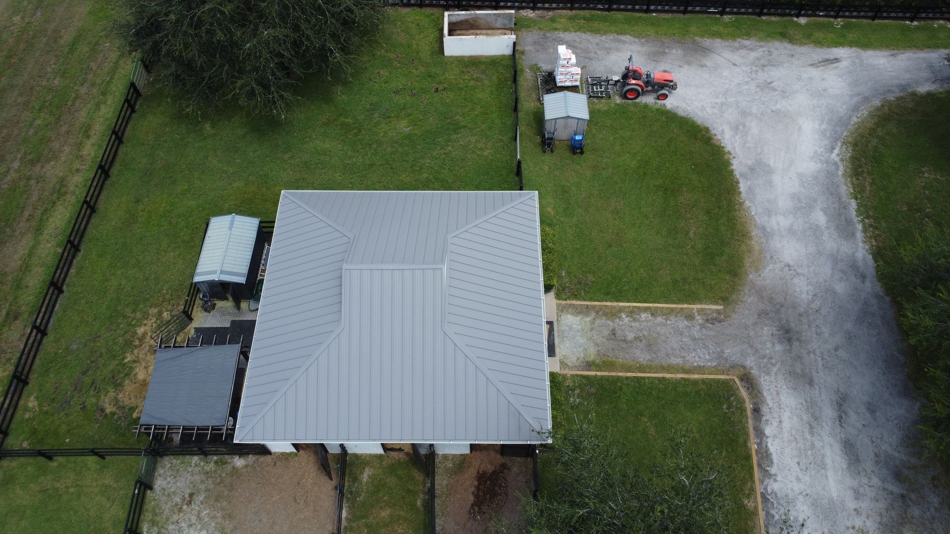 Aerial view of a house with a gray metal roof, gravel driveway, and grassy yard.