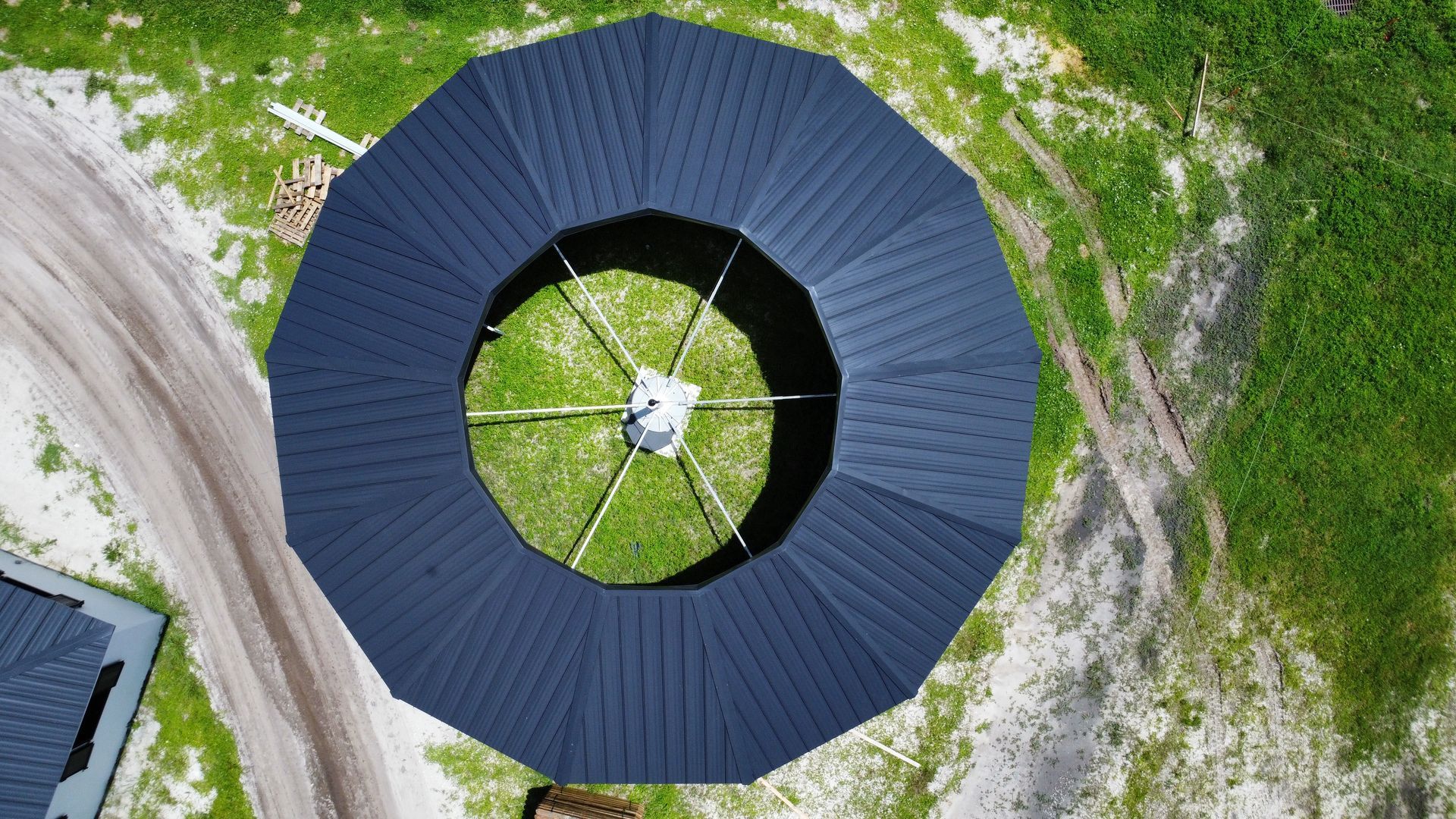 Aerial view of a circular dark-roofed structure surrounded by grass and a winding dirt road