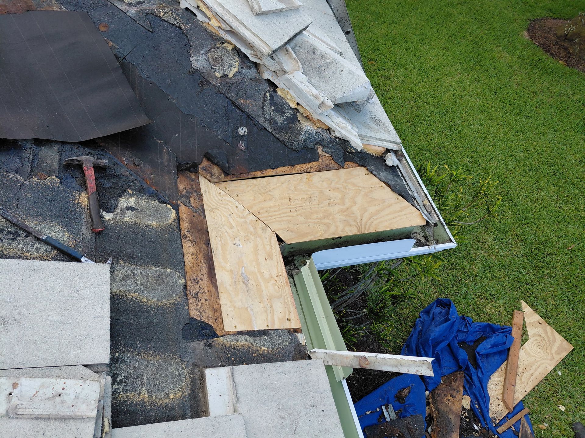 Roof repair with exposed plywood, shingles, and blue tarp on a house roof