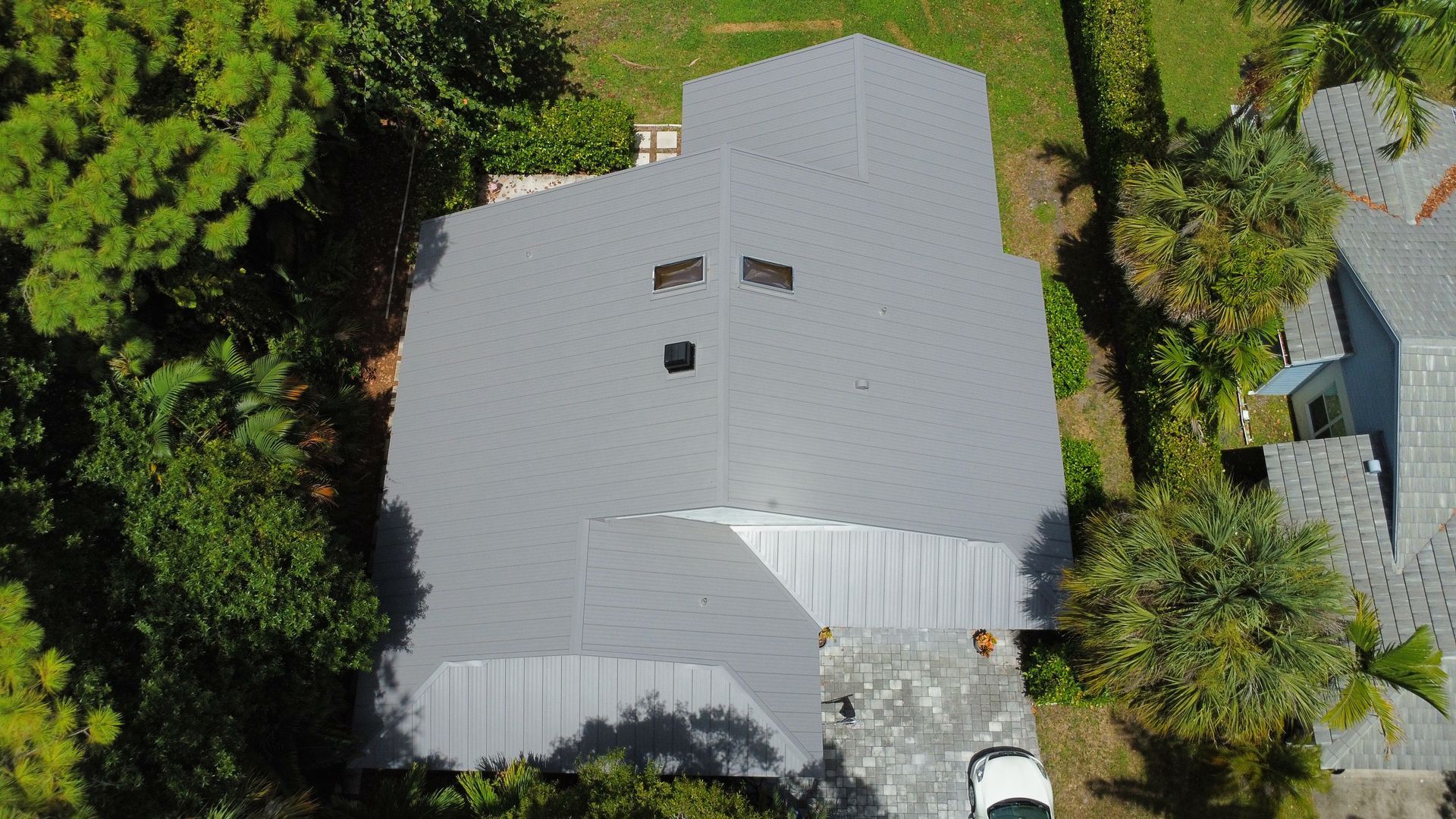 Aerial view of a gray metal-roofed house surrounded by dense green trees.