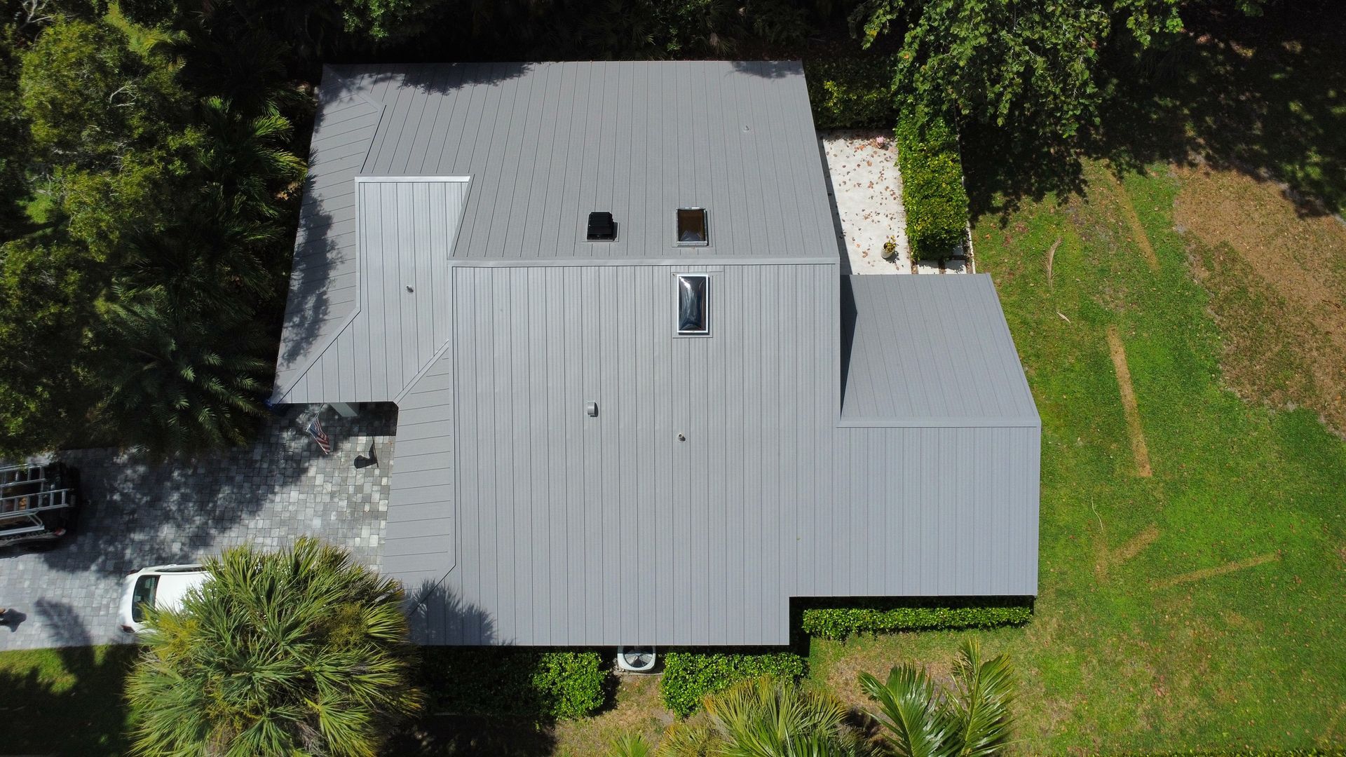 Aerial view of a gray metal-roofed house surrounded by trees and grass
