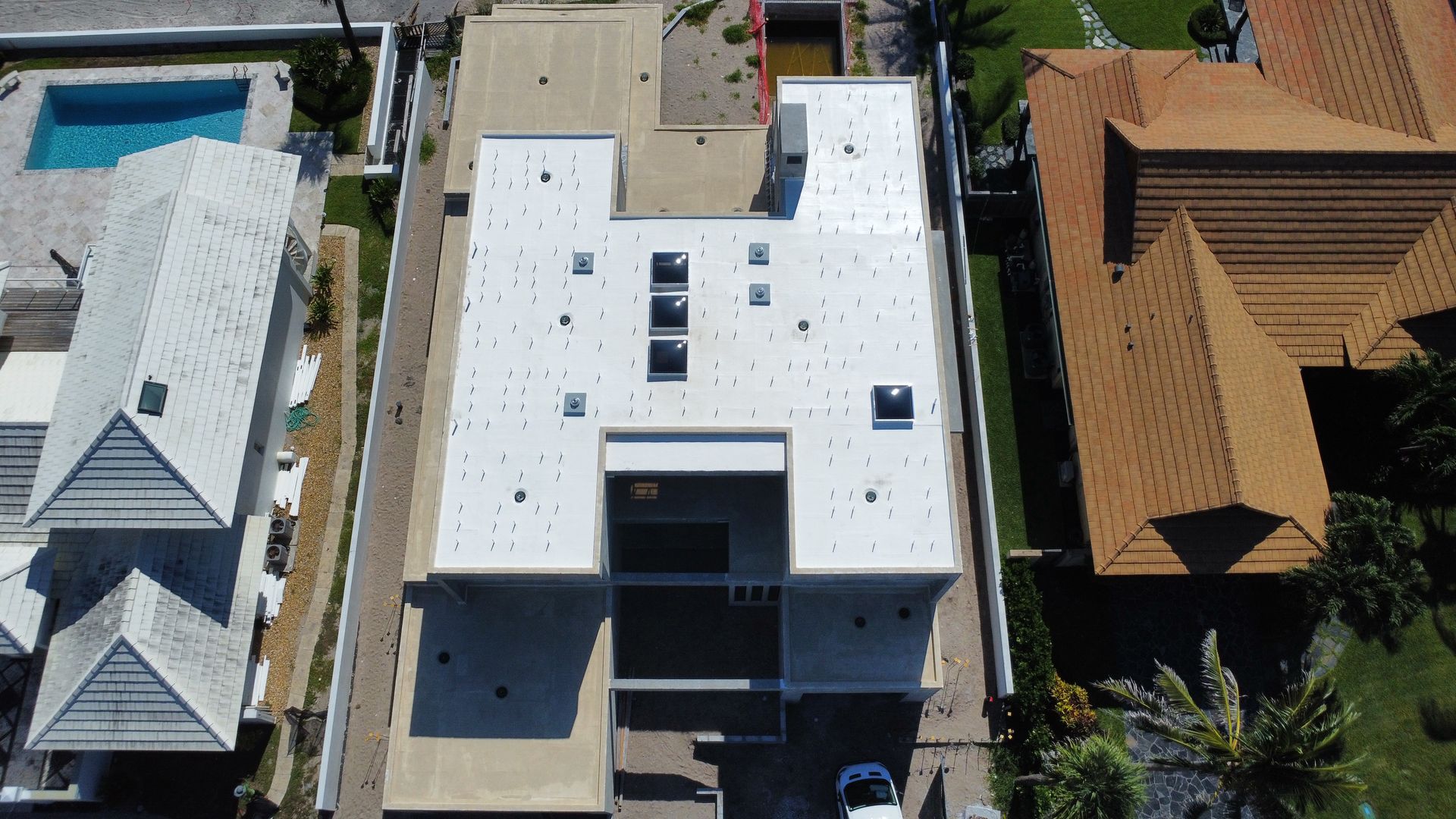 Aerial view of a white-roofed building between neighboring houses with red and gray roofs.