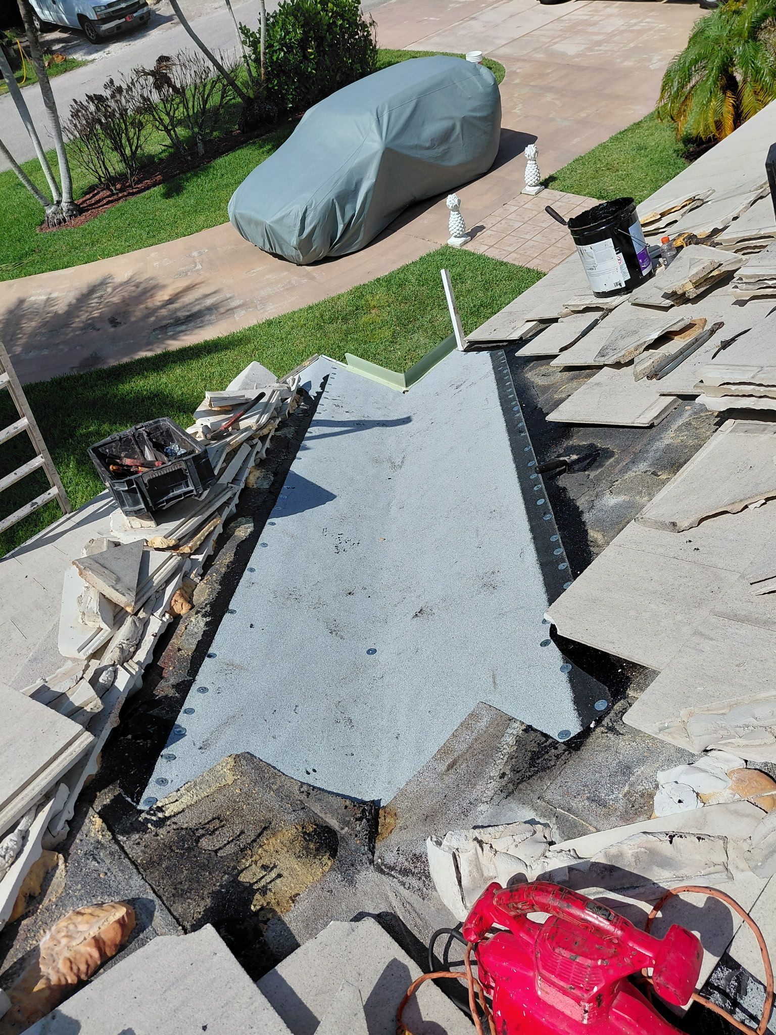 Stone walkway under construction beside a driveway, with a covered car and scattered building materials nearby