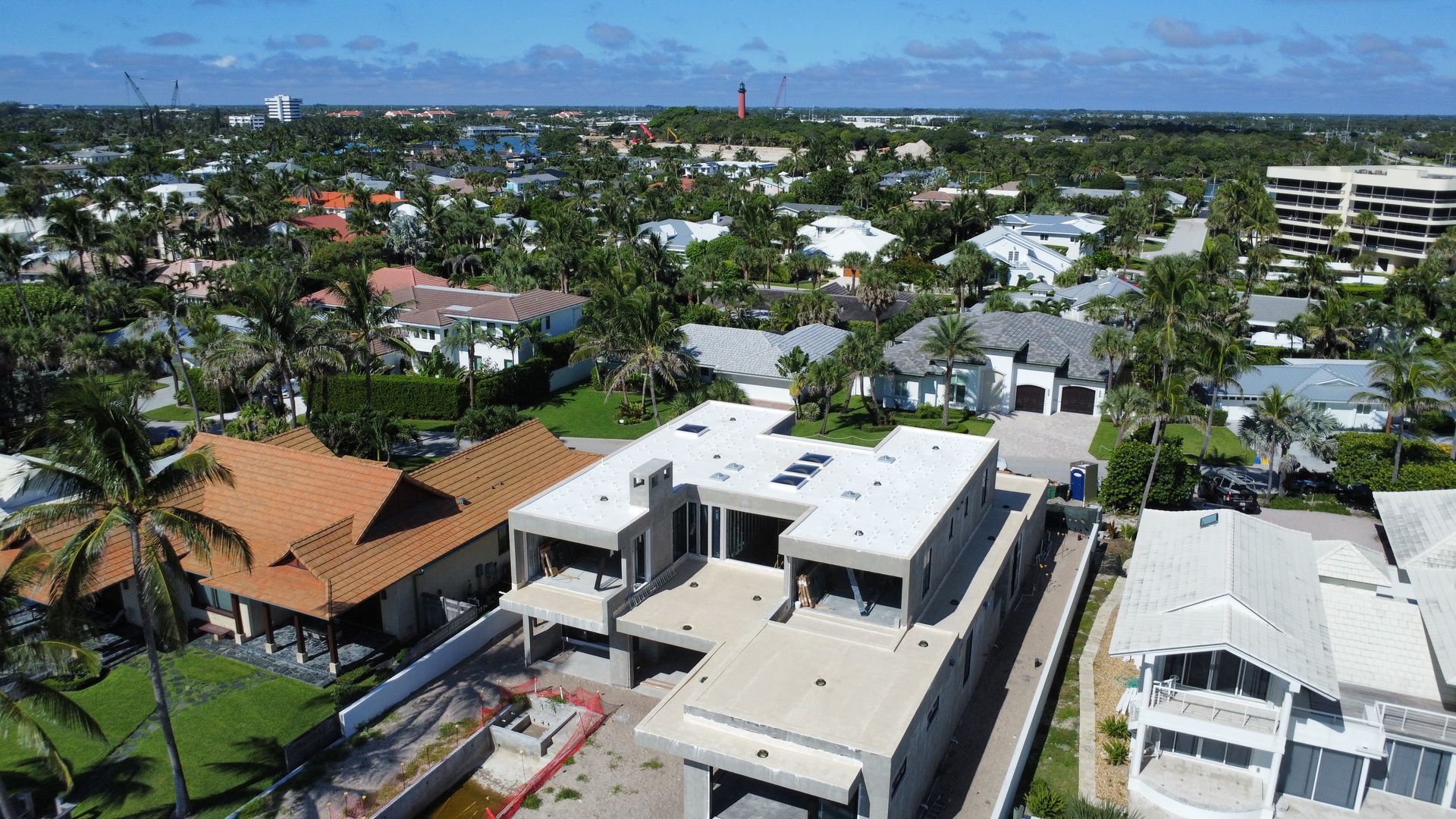Aerial view of a coastal neighborhood with white buildings, palm trees, and the ocean on the horizon.