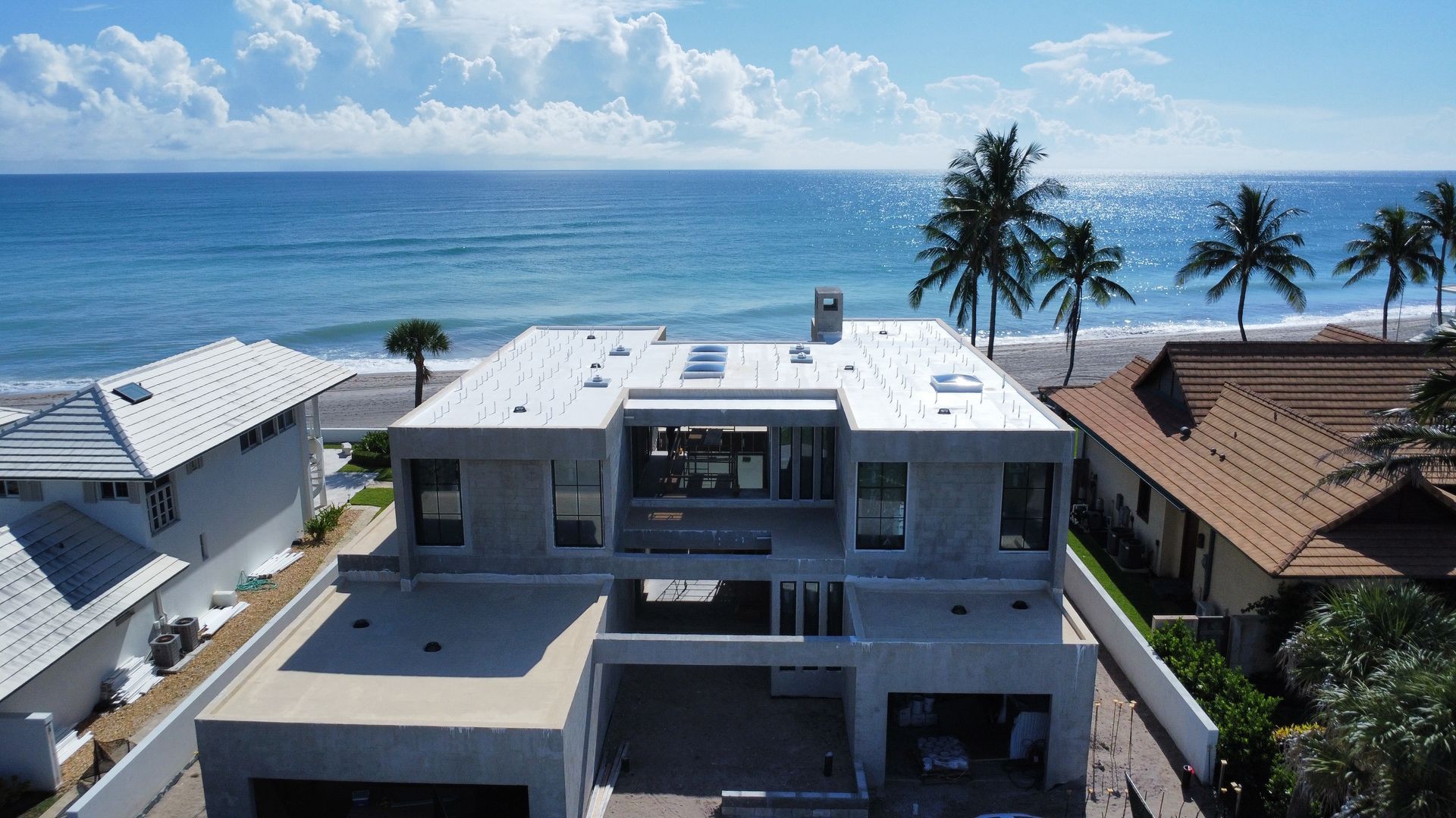Modern gray beachfront house with rooftop deck overlooking palm trees and the ocean