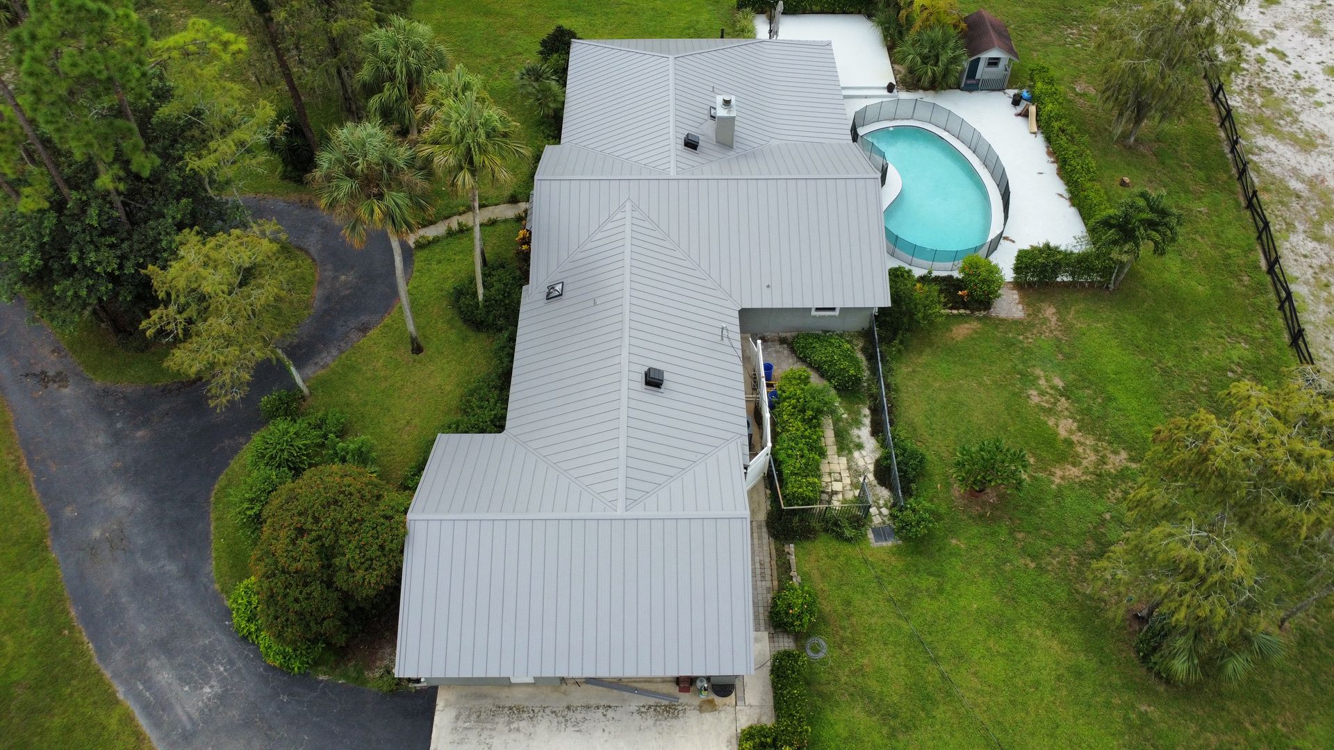 Aerial view of a gray-roofed house with a curved backyard swimming pool and green lawn.