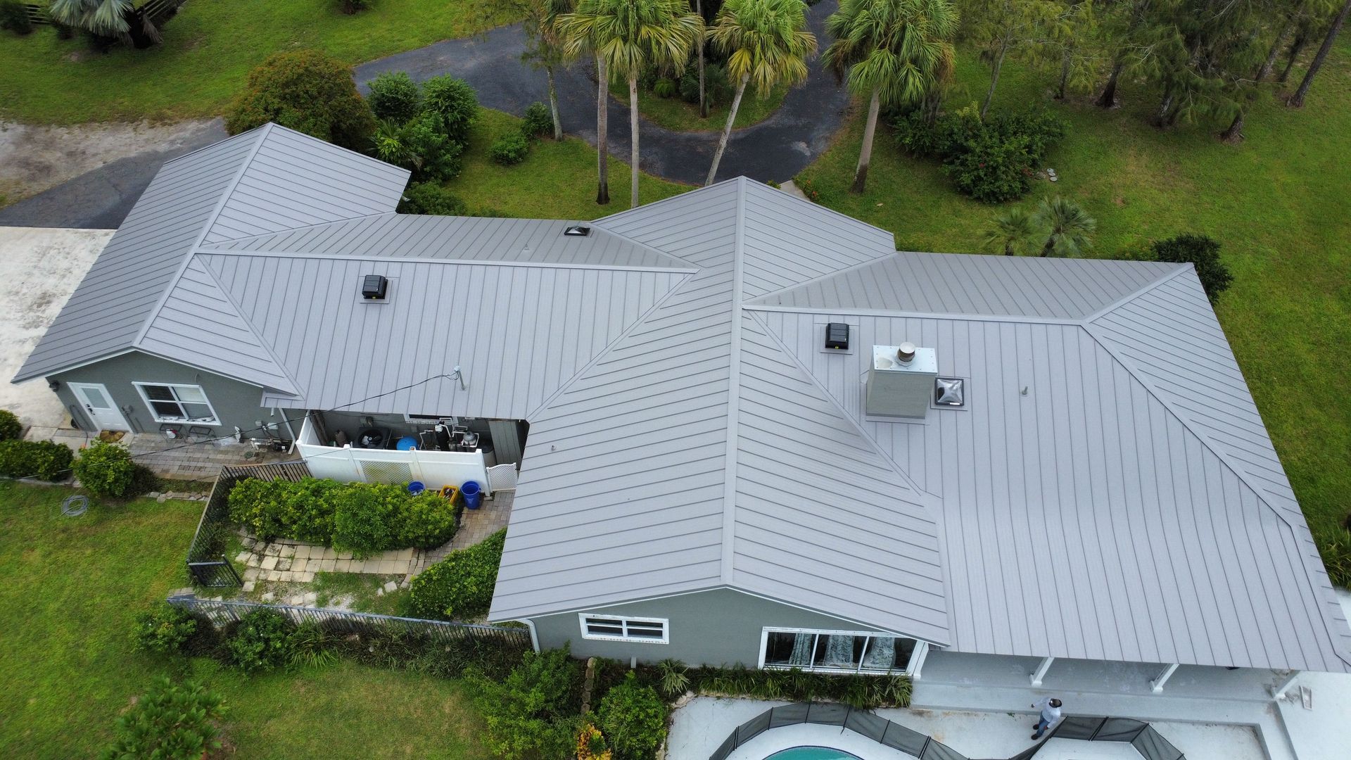 Aerial view of a gray-roofed house surrounded by green trees and lawn.