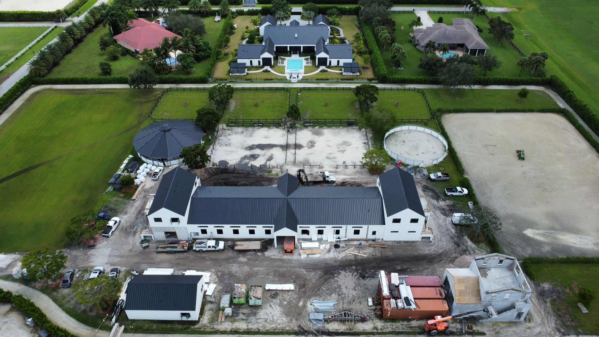 Aerial view of a large white building under construction beside green fields and nearby homes