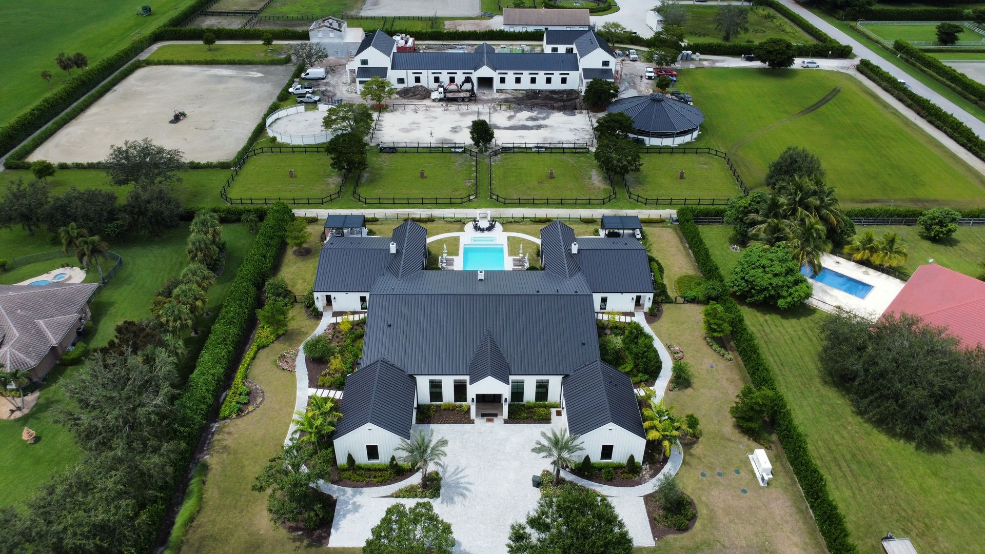 Aerial view of a large white estate with a blue pool, surrounded by green fields and water channels.