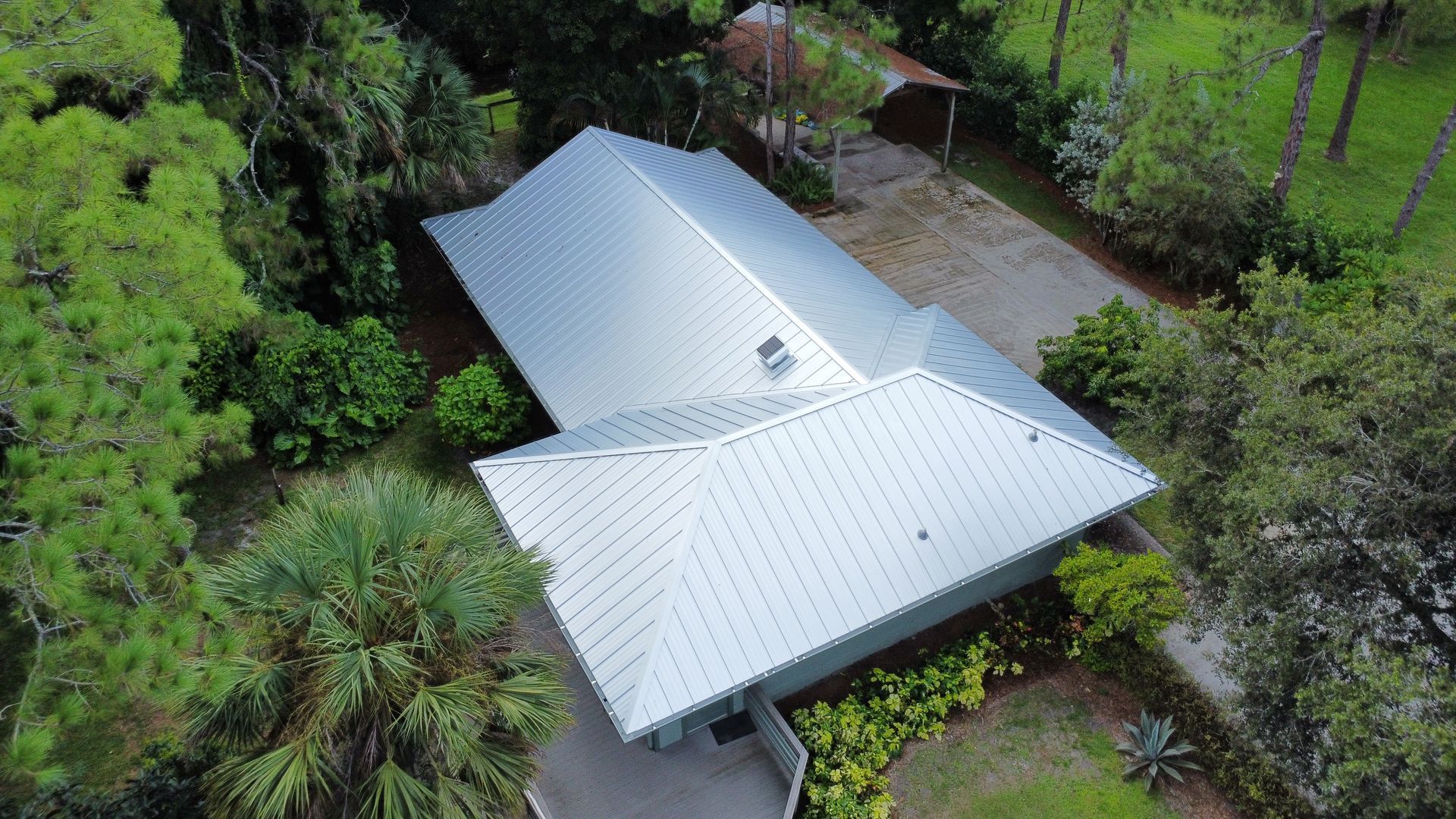 Aerial view of a gray-roofed house surrounded by dense green trees and landscaping.