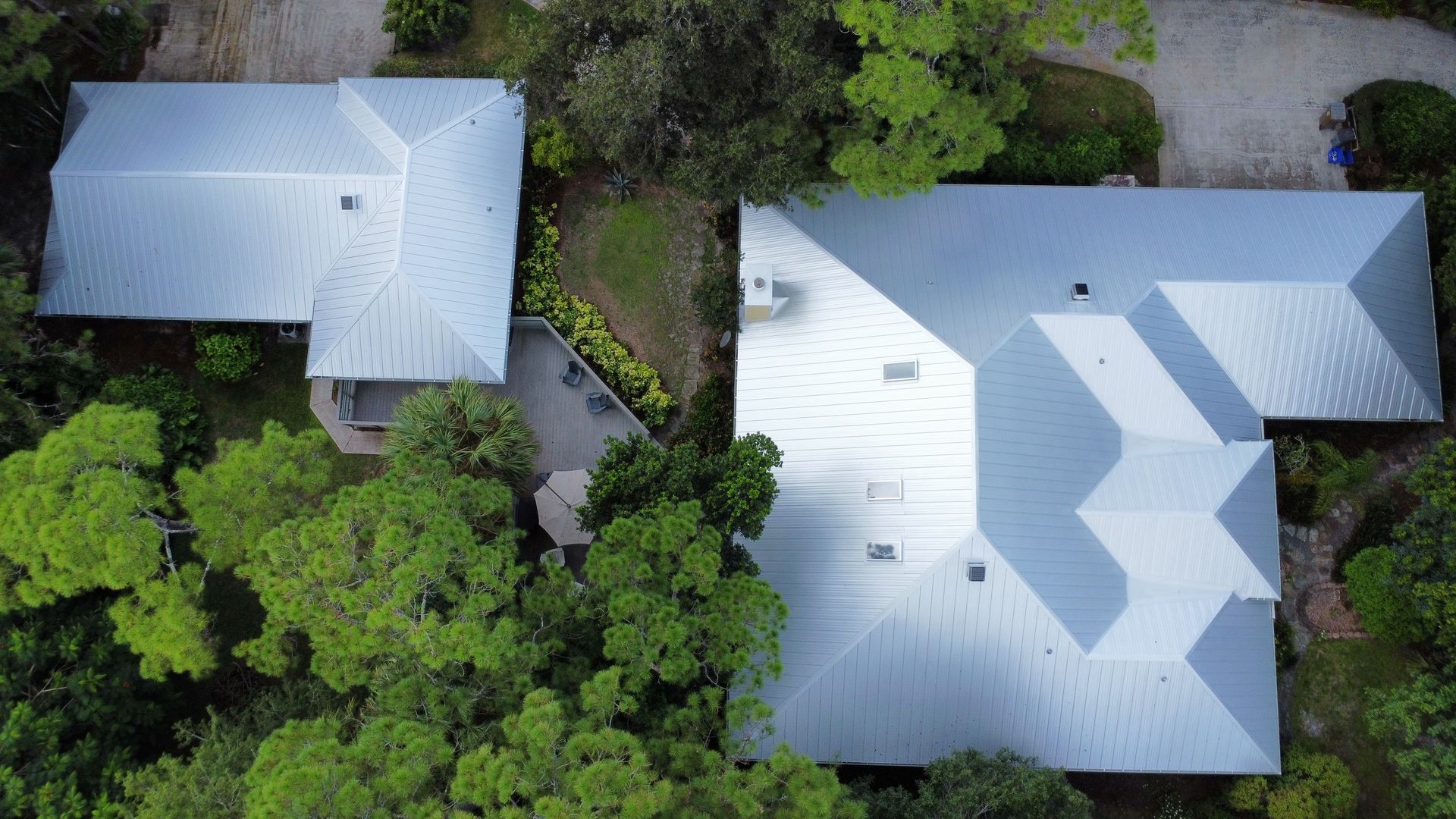 Aerial view of two white-roofed houses surrounded by dense green trees and shrubs.