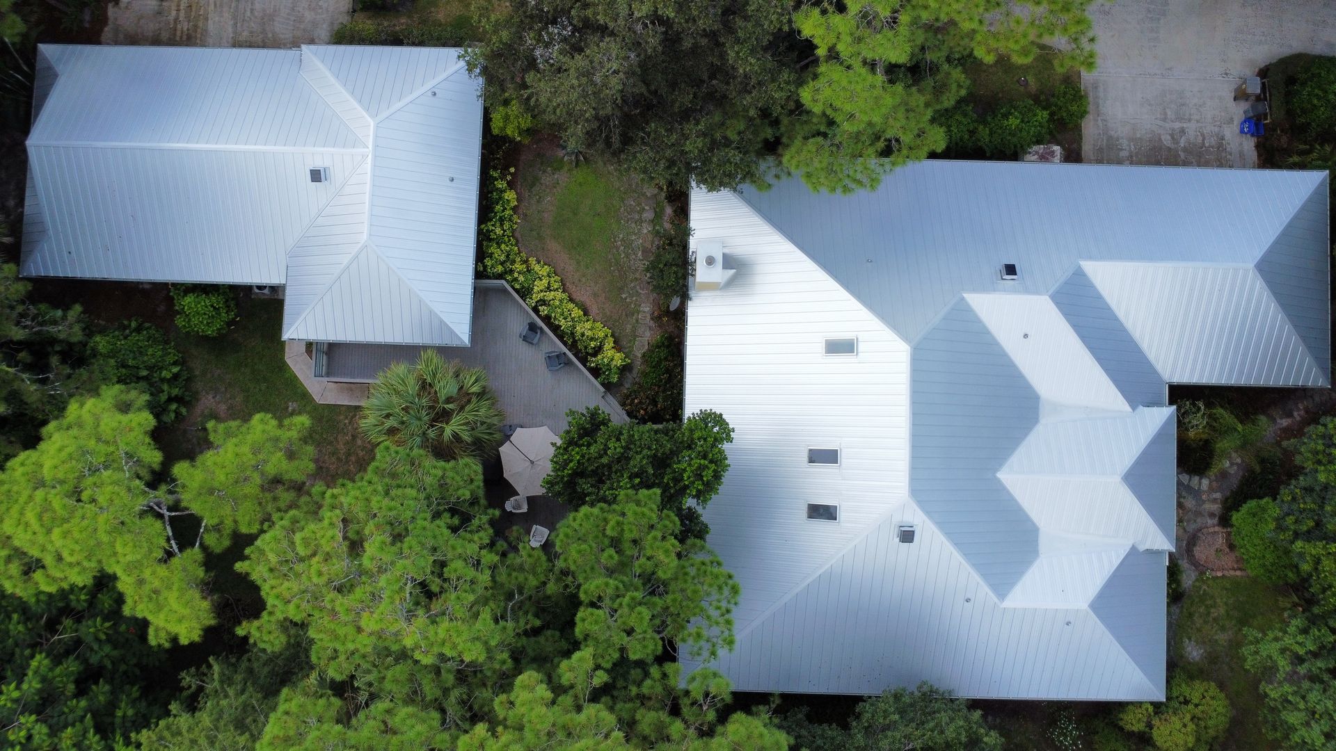 Aerial view of two white-roofed houses surrounded by dense green trees and foliage.