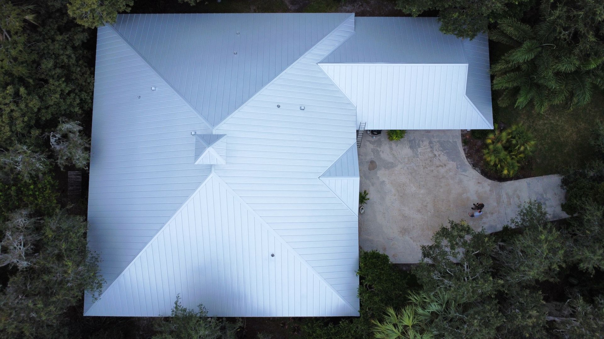 Overhead view of a light gray roof with a small patio and surrounding trees.