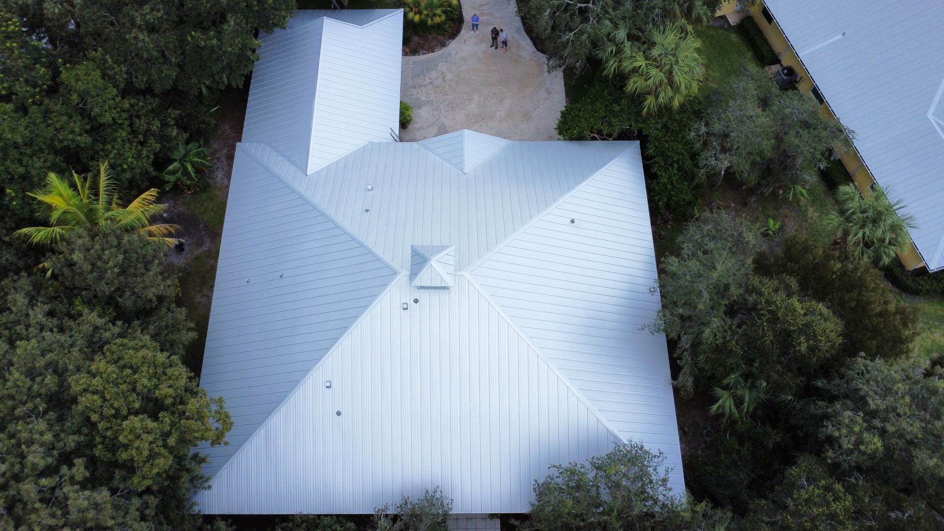 Aerial view of a white metal-roof house surrounded by trees and greenery