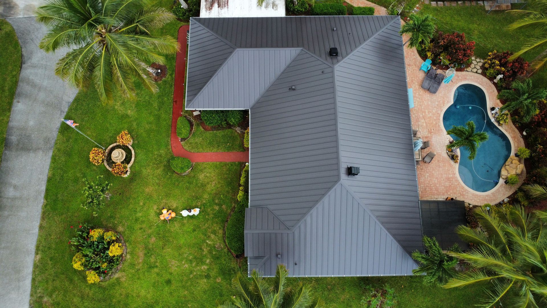 Aerial view of a house with a gray roof, green lawn, and a kidney-shaped blue pool.
