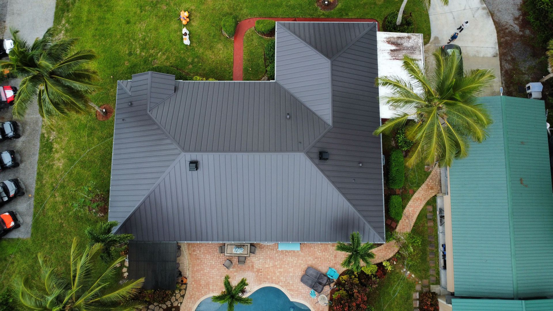 Aerial view of a gray-roofed house surrounded by palm trees and a backyard pool