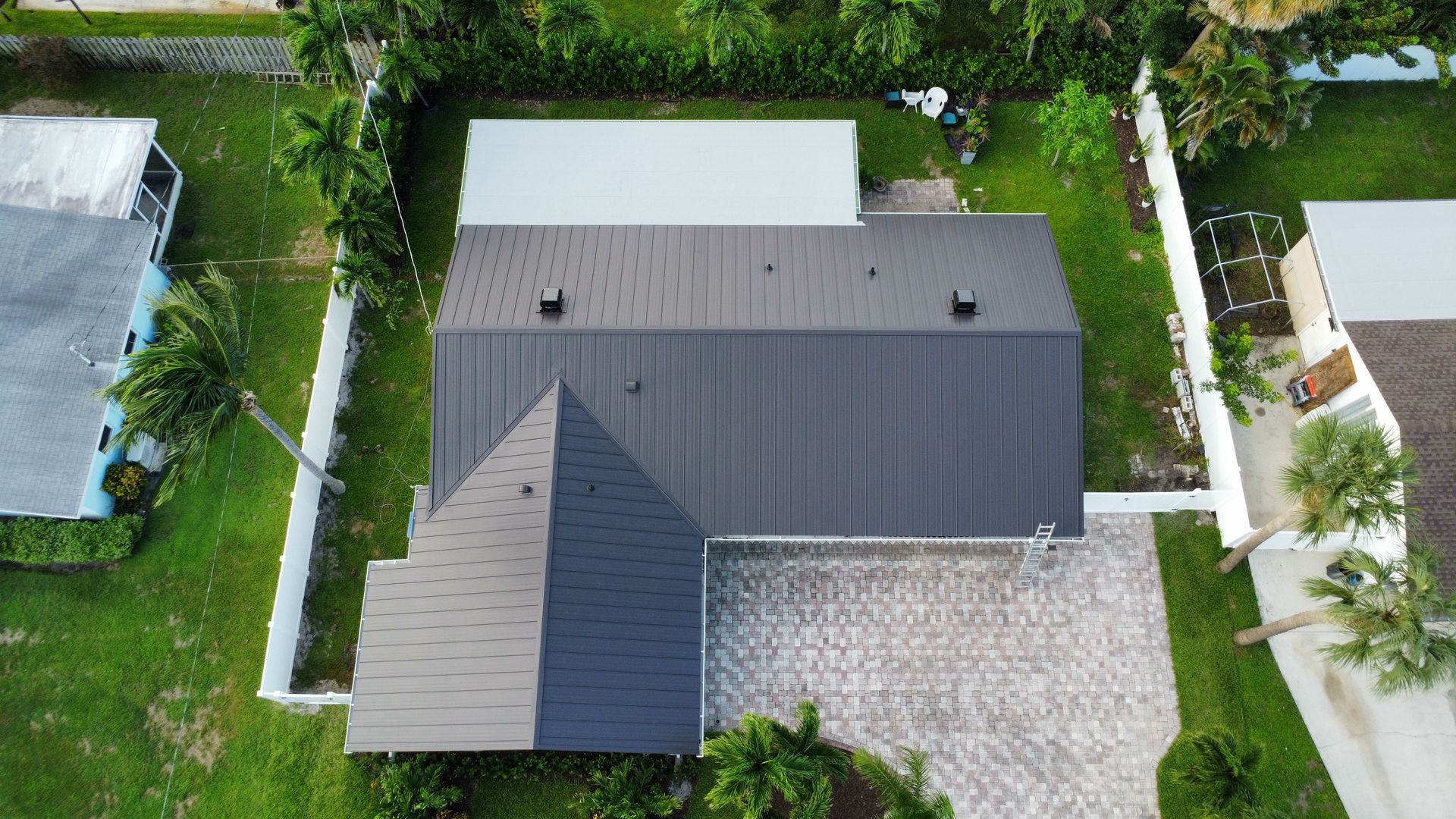 Aerial view of a modern house with a dark roof, white walls, and a driveway surrounded by greenery.