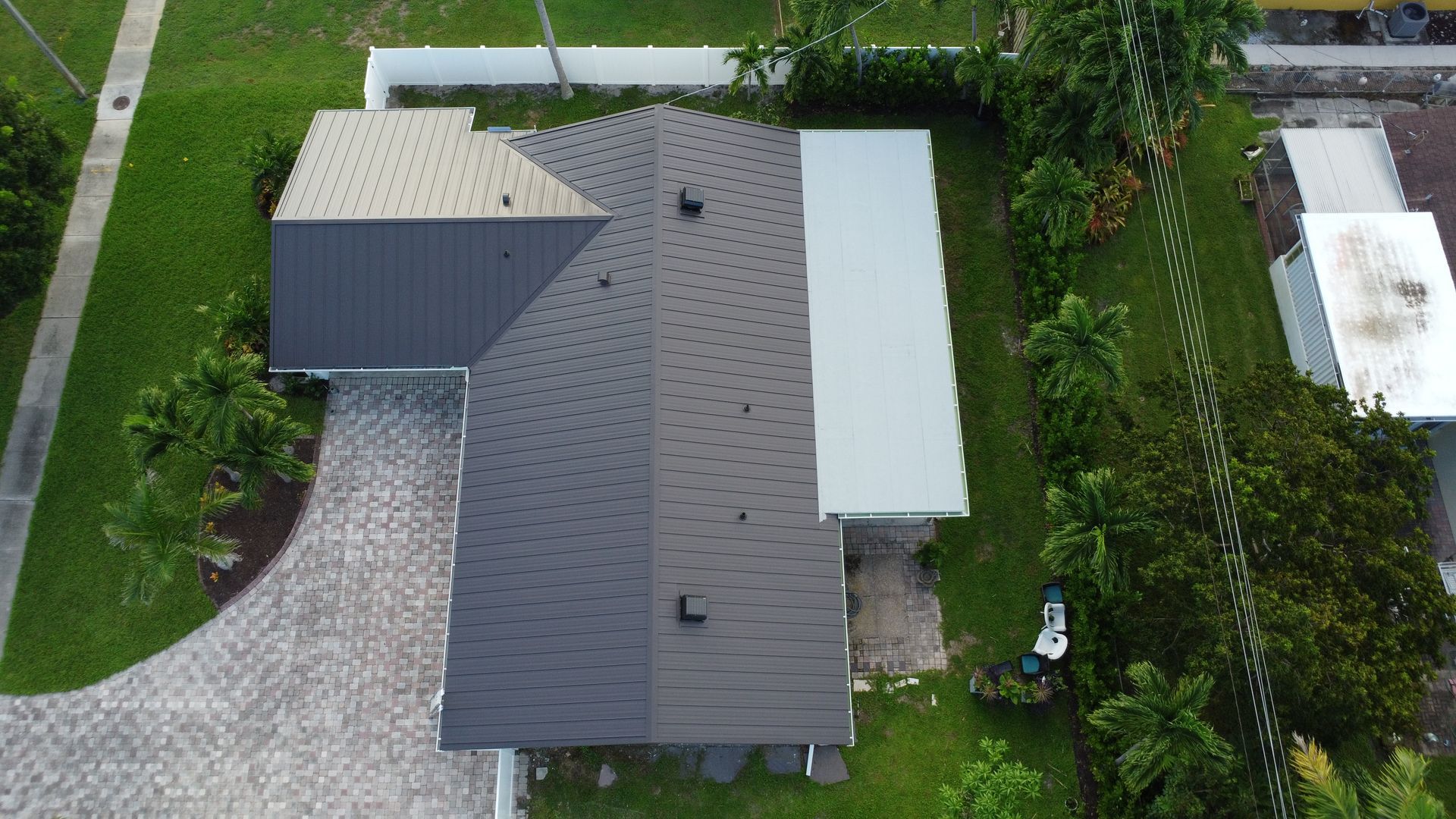 Aerial view of a gray-roofed house with a driveway, yard, and trees around it.