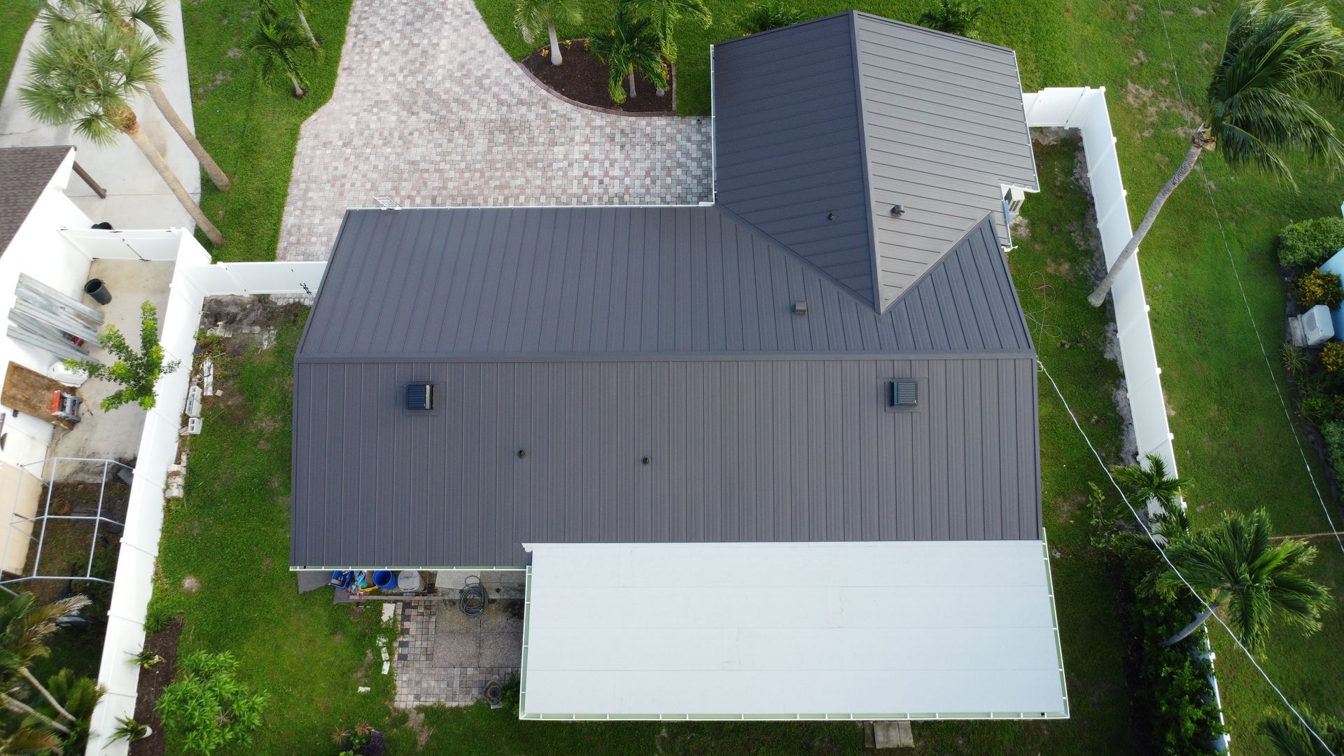 Aerial view of a house with a dark gray roof, white patio cover, and surrounding greenery.