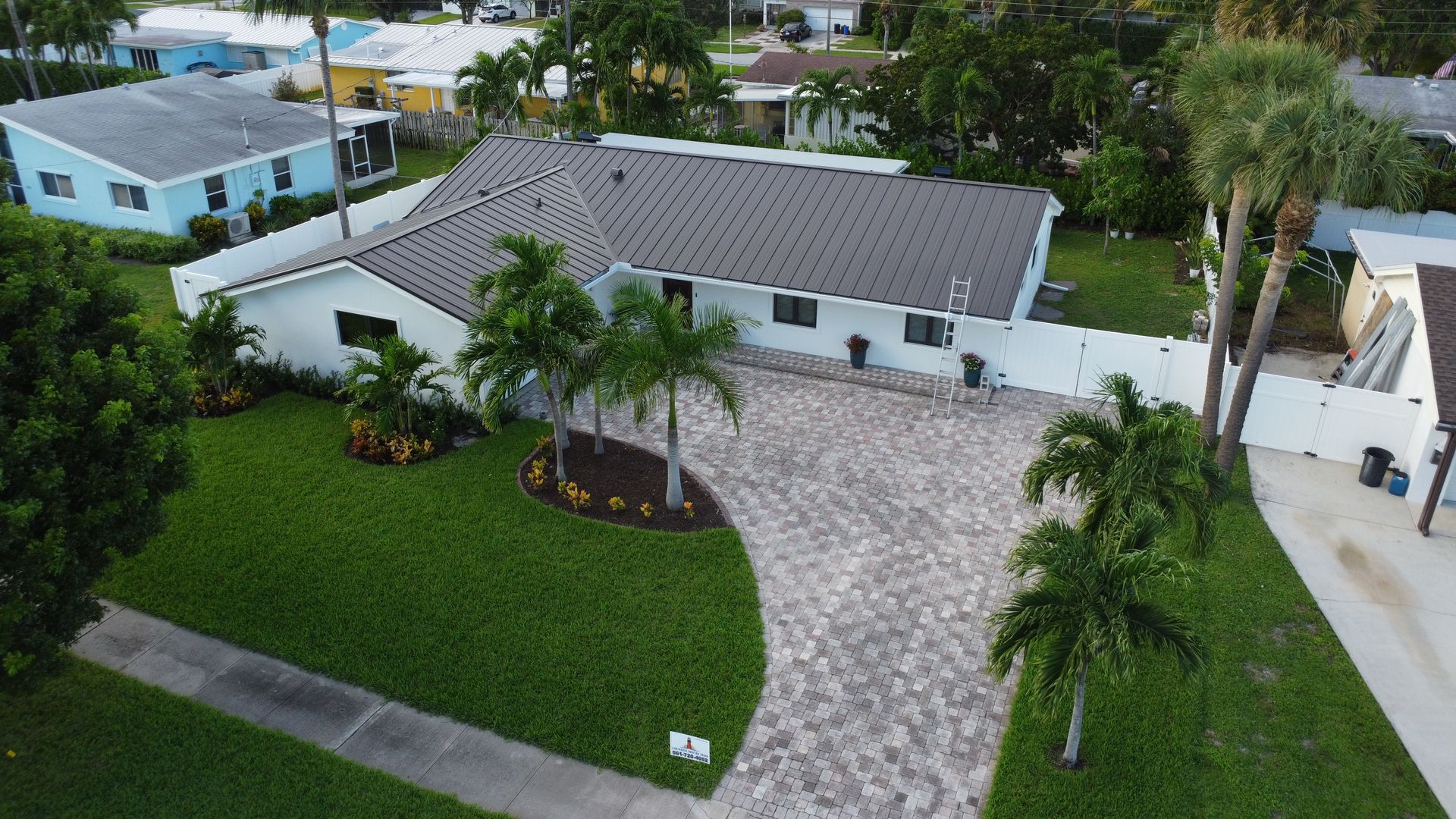 Aerial view of a white house with a gray roof, curved driveway, and lush green landscaping.