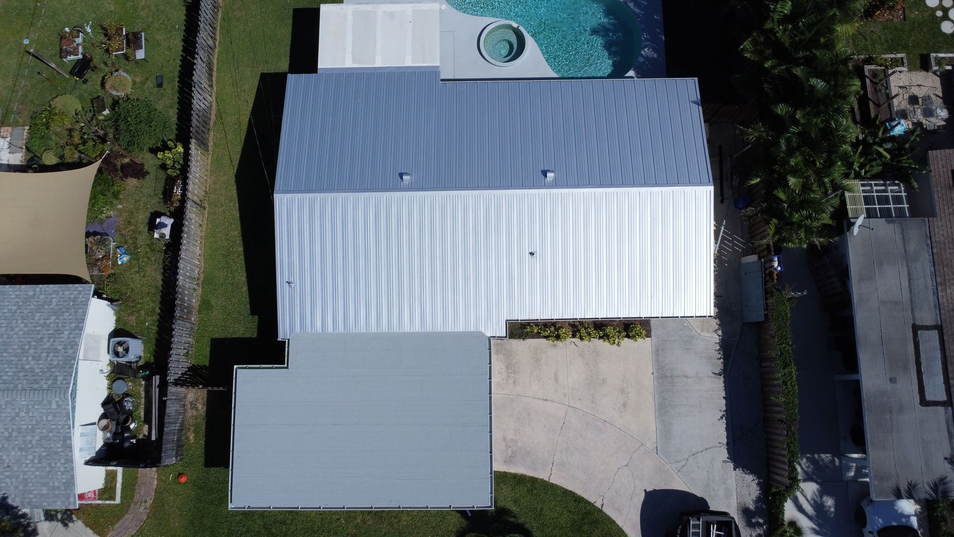 Aerial view of a house with a white metal roof, driveway, and backyard pool.