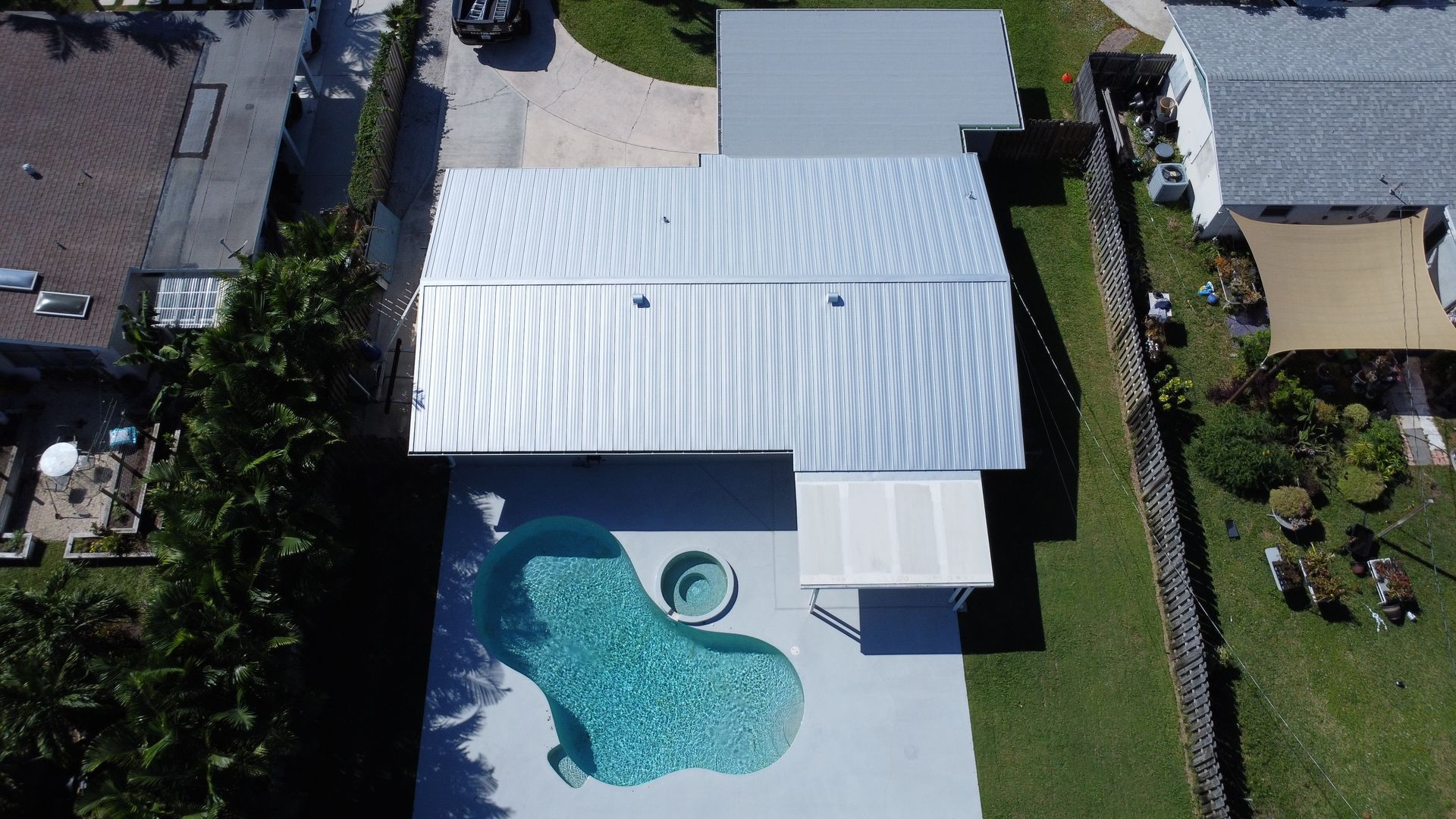 Aerial view of a house with a white roof and backyard pool with a spa and patio.