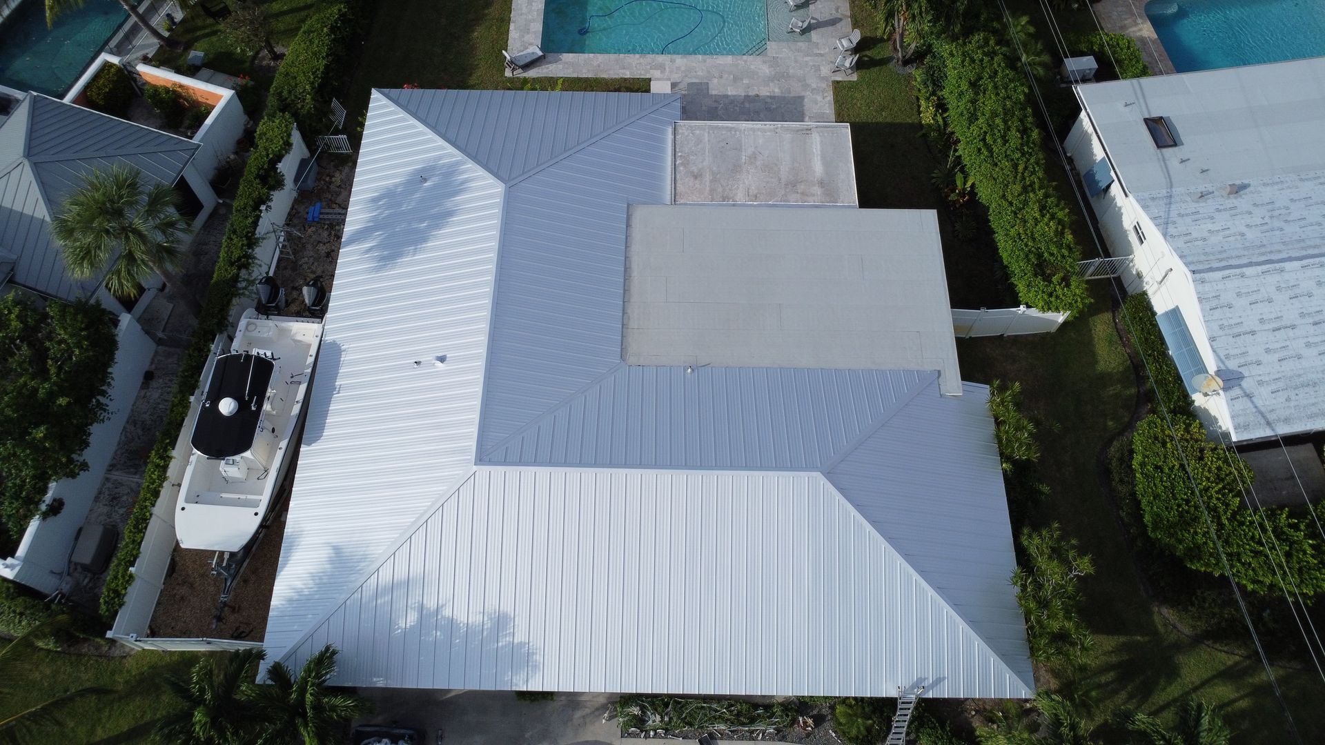 Aerial view of a white-roofed house surrounded by trees and neighboring homes.