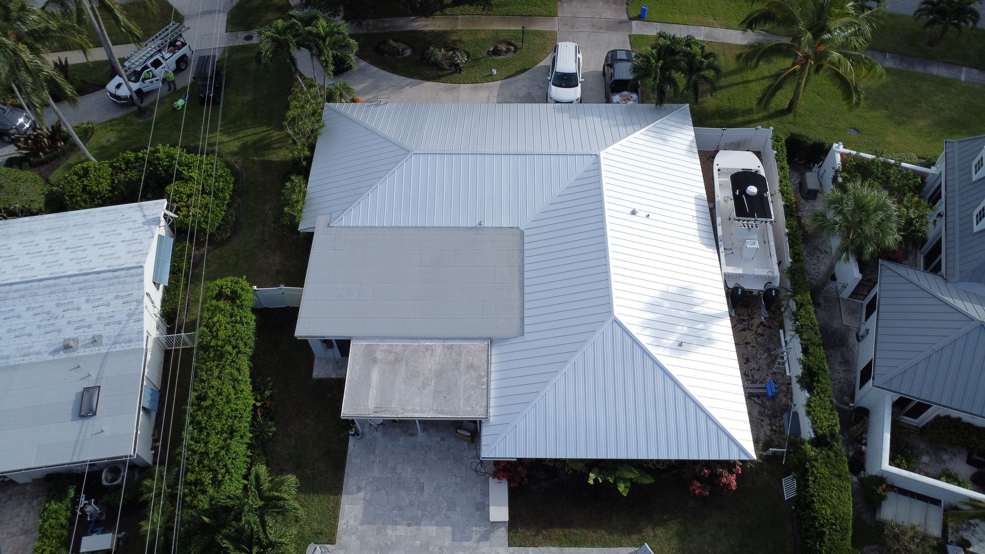 Aerial view of a white-roofed house with a driveway and palm trees in a residential neighborhood