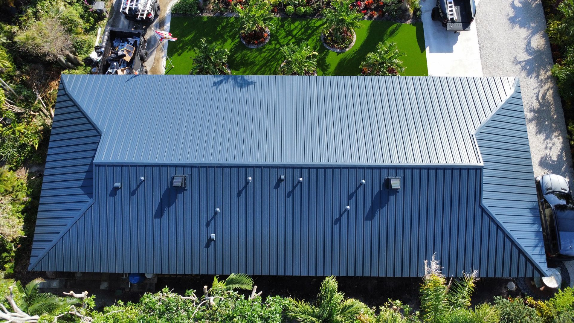 Top-down view of a gray metal-roofed building surrounded by trees and grass
