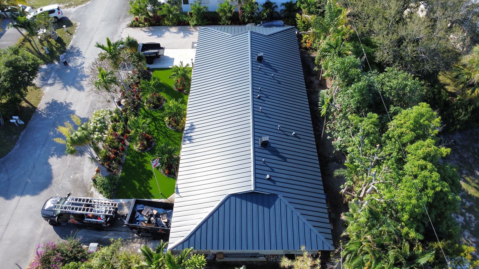 Aerial view of a gray-roofed house surrounded by trees, with a vehicle parked beside it.