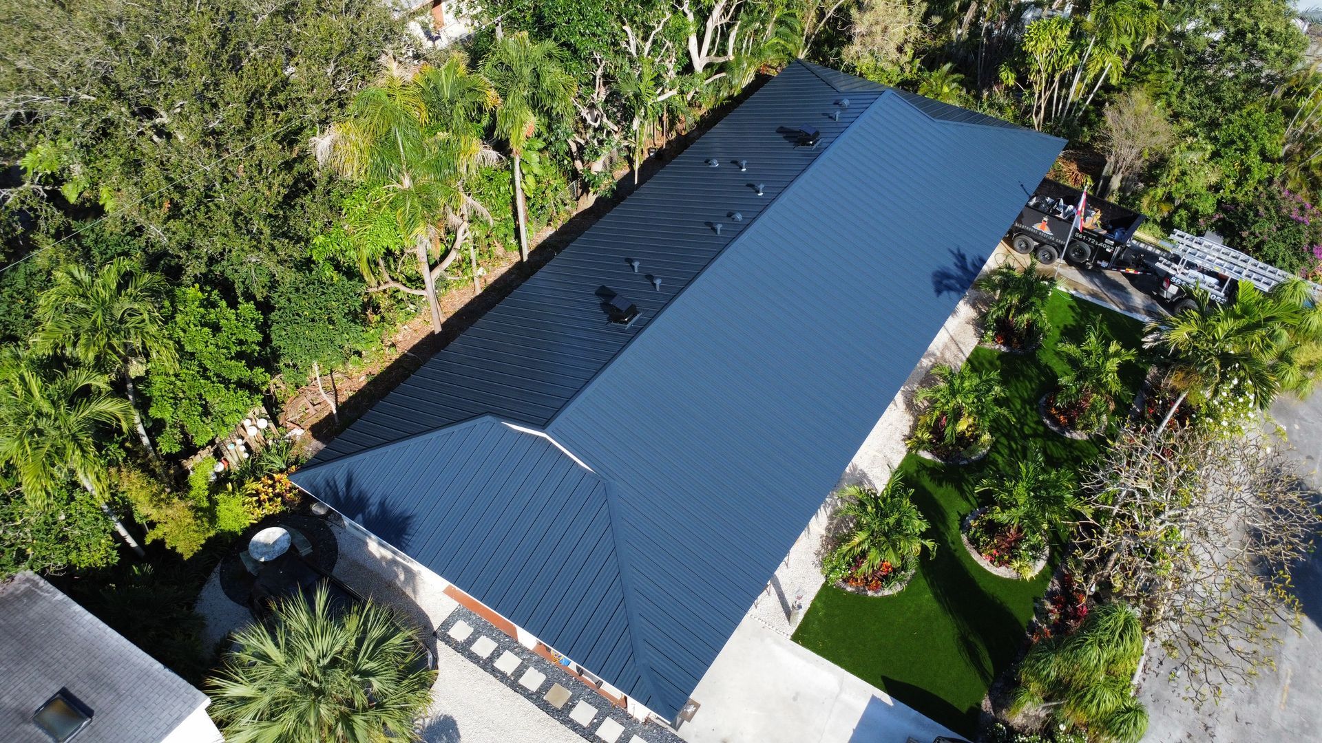 Aerial view of a house with a dark roof surrounded by green trees and garden landscaping