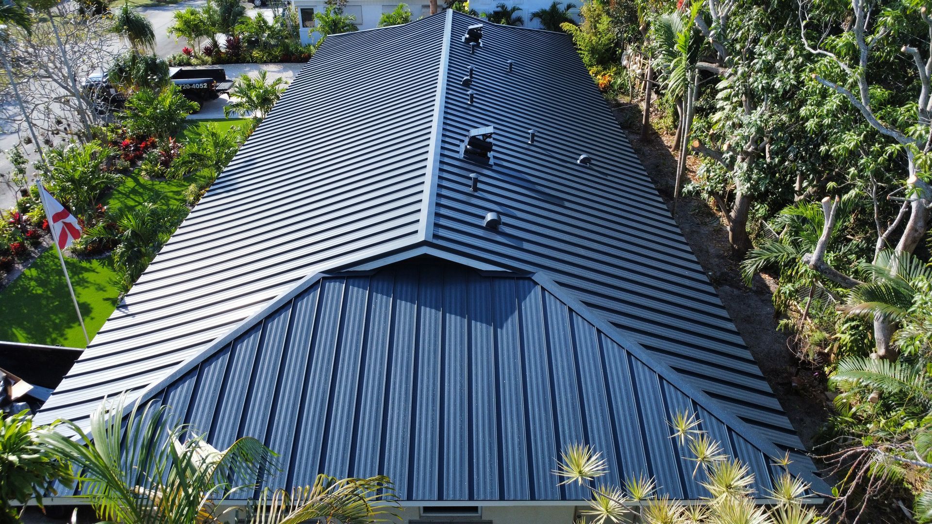 Black metal roof with curved ridges on a house, surrounded by lush green trees and garden