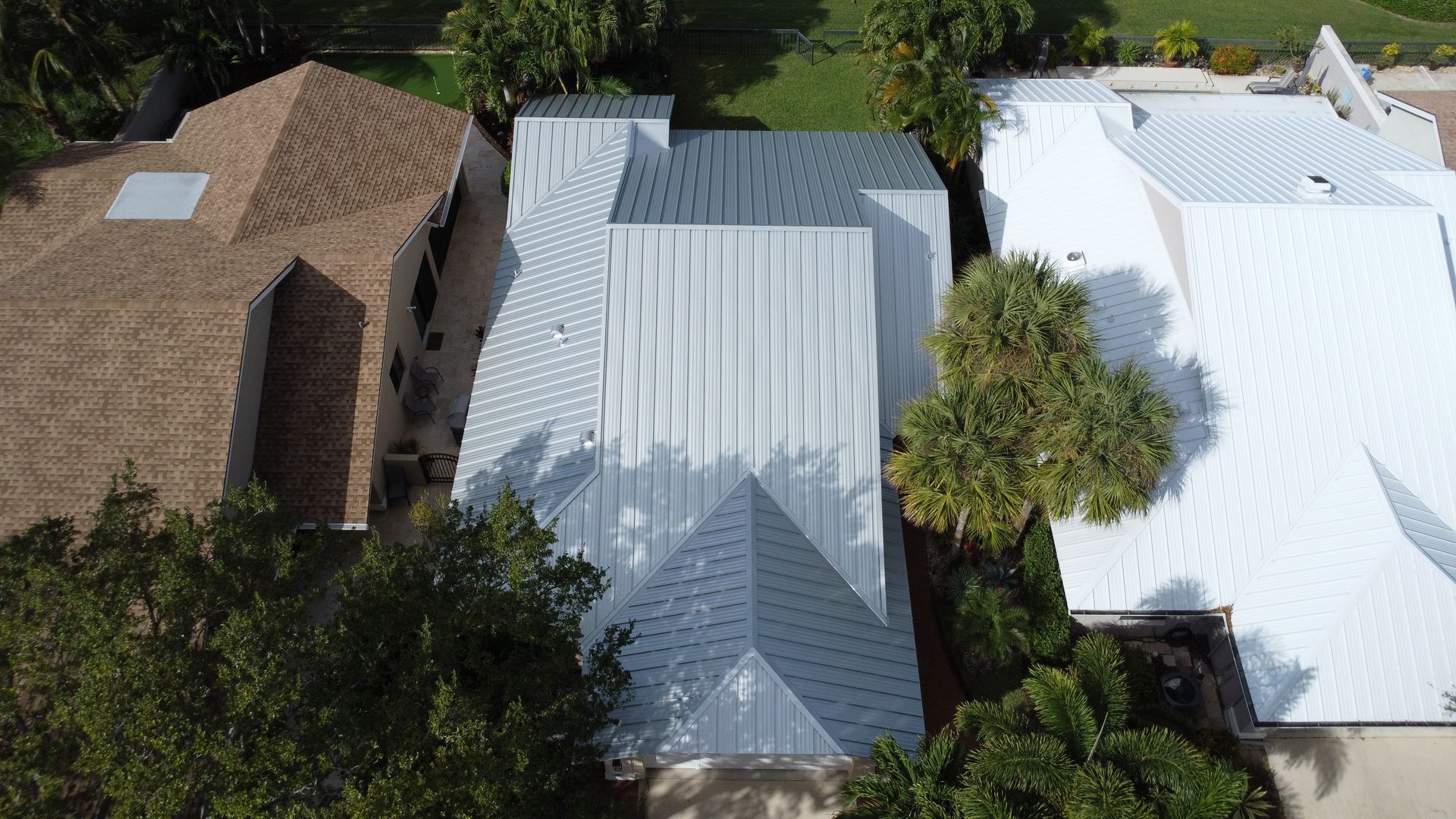 Aerial view of three houses with brown, gray, and white roofs surrounded by trees and greenery