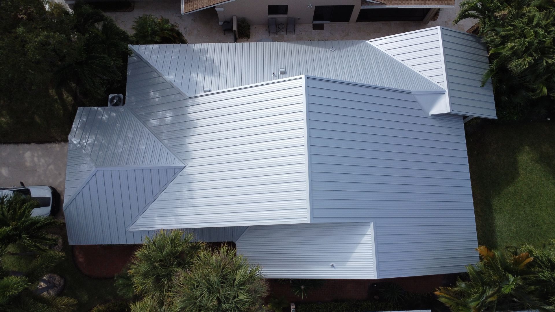 Aerial view of a house with a light gray metal roof surrounded by trees and a driveway.
