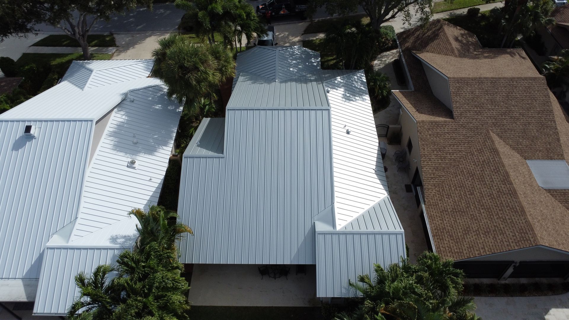 Aerial view of neighboring houses with white, gray, and brown roofs surrounded by trees.