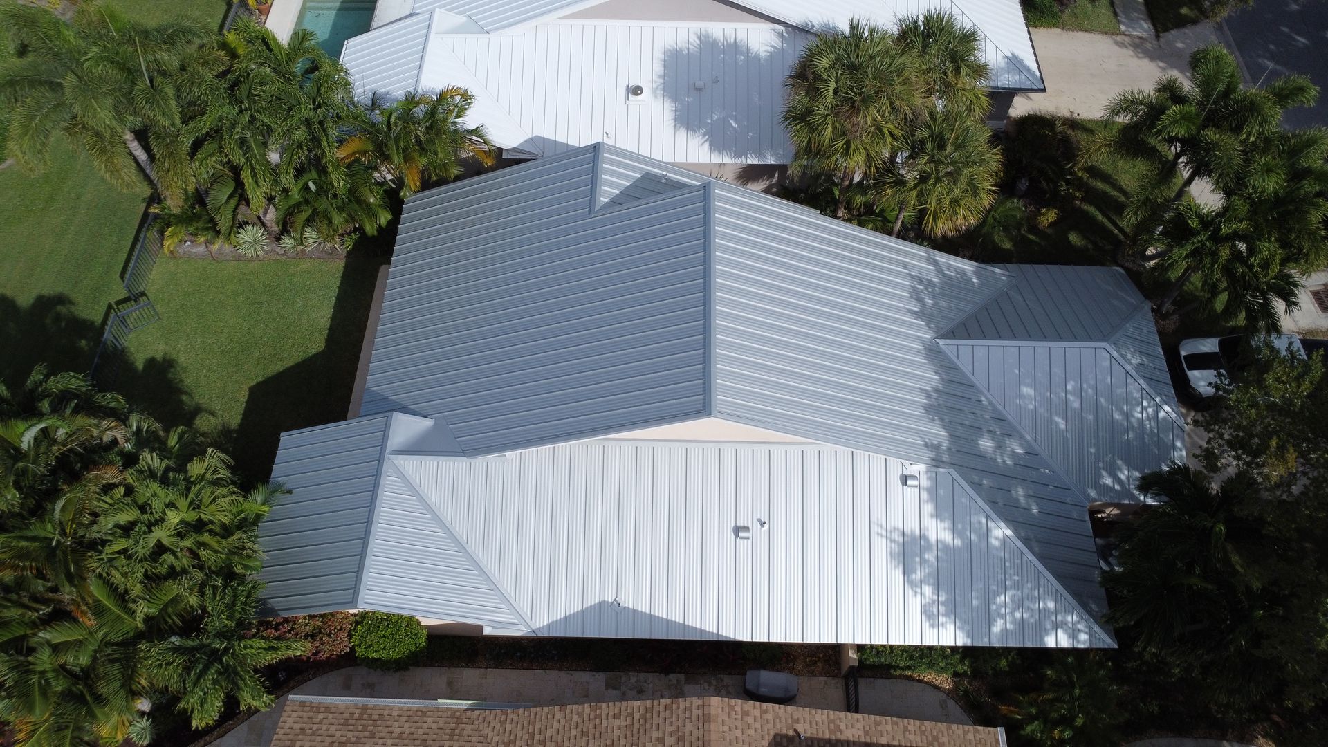 Aerial view of a white-roofed house surrounded by palm trees and greenery