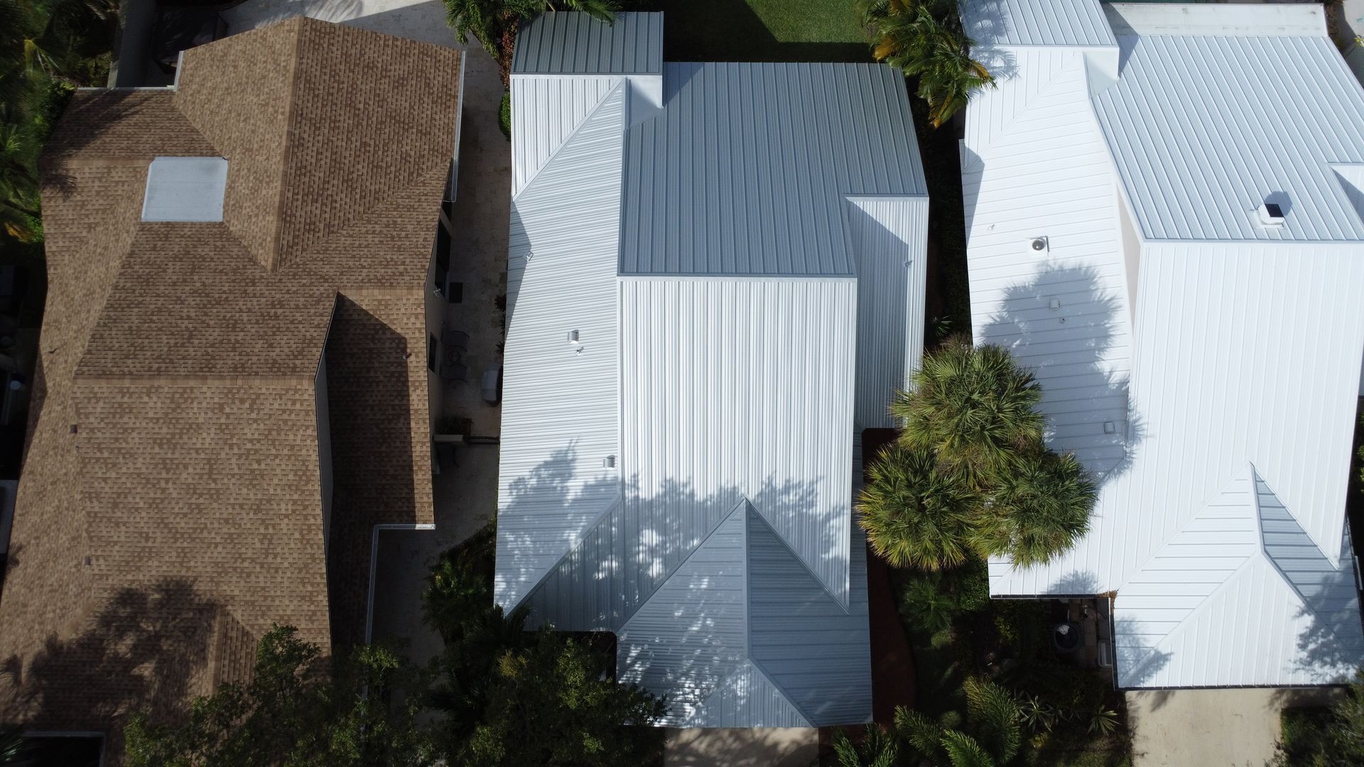 Aerial view of three adjacent houses with brown, gray, and white roofs in a residential neighborhood