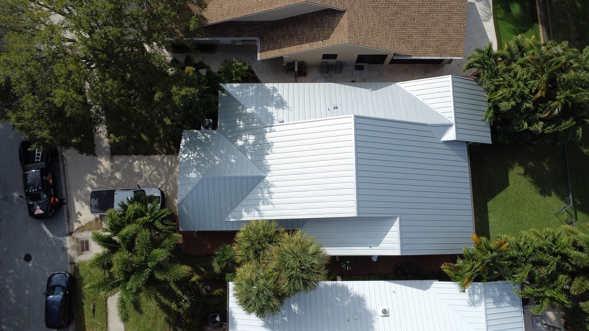 Aerial view of white-roofed houses, trees, and parked cars on a residential street