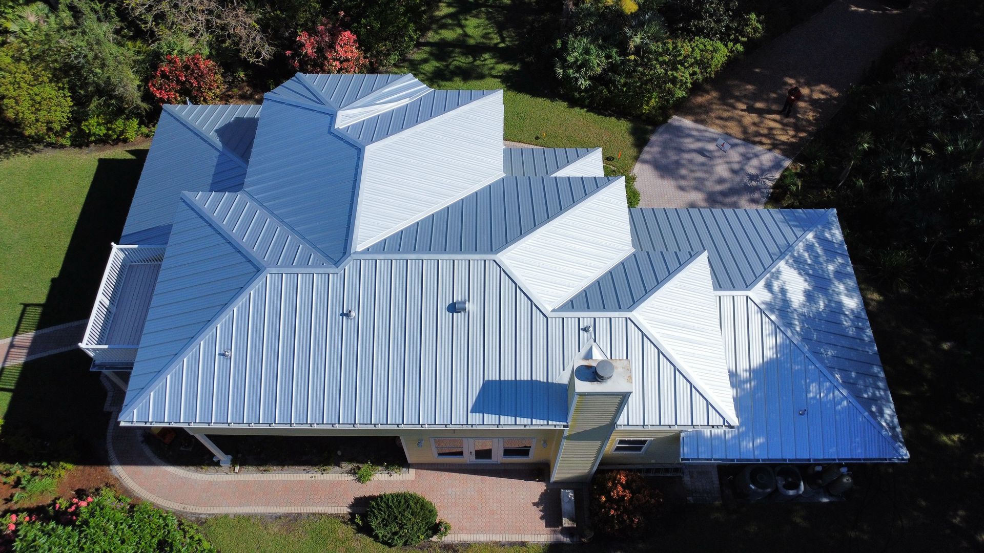 Aerial view of a house with a shiny metal roof and surrounding green yard