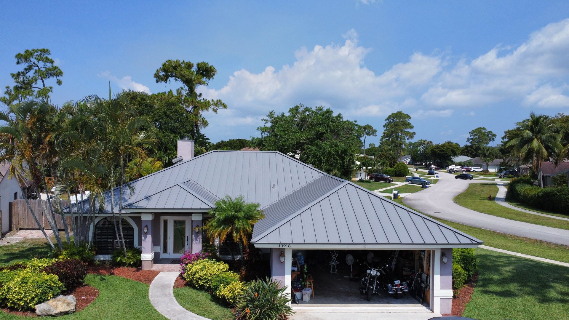 Single-story house with gray roof, white garage, and landscaped front yard in a sunny suburban neighborhood