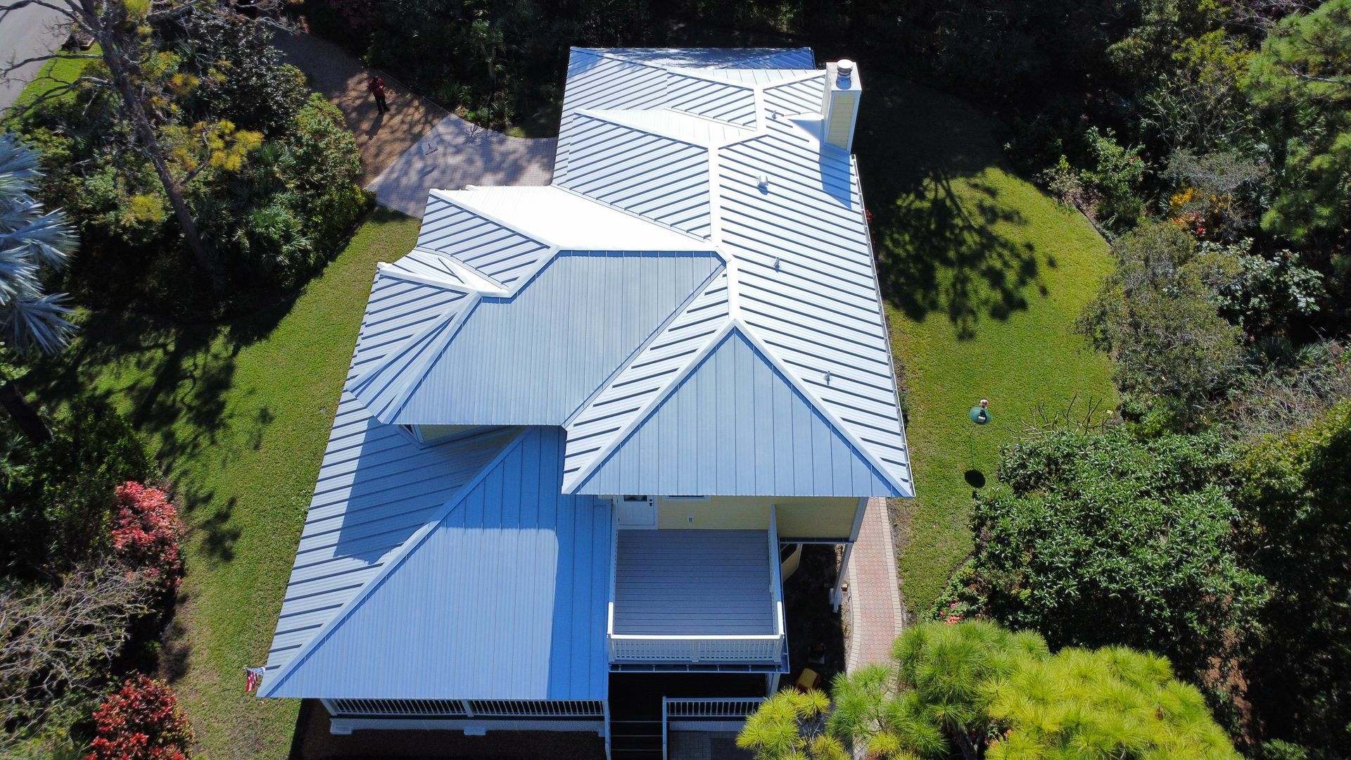 Aerial view of a white metal-roofed house surrounded by lush green trees and lawn