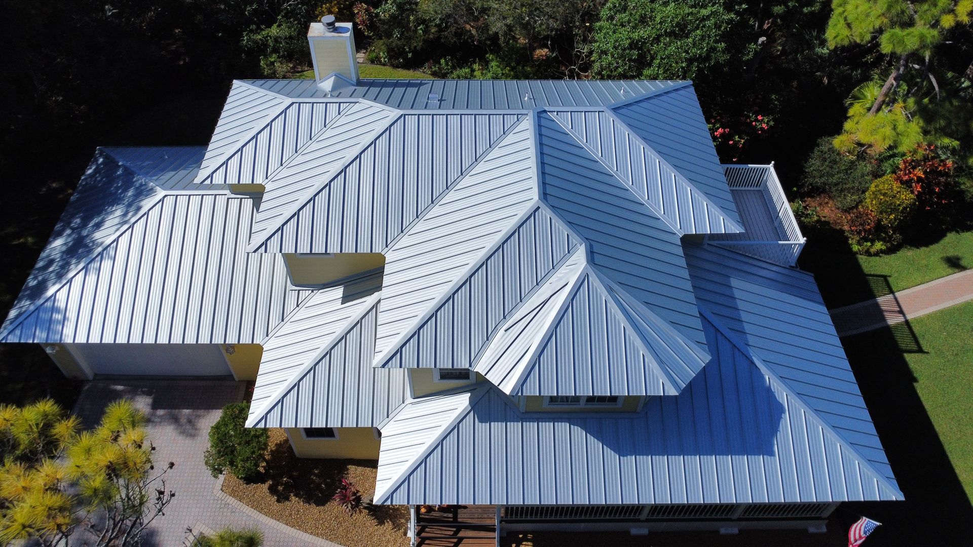 Aerial view of a house with a silver metal roof surrounded by trees and a driveway