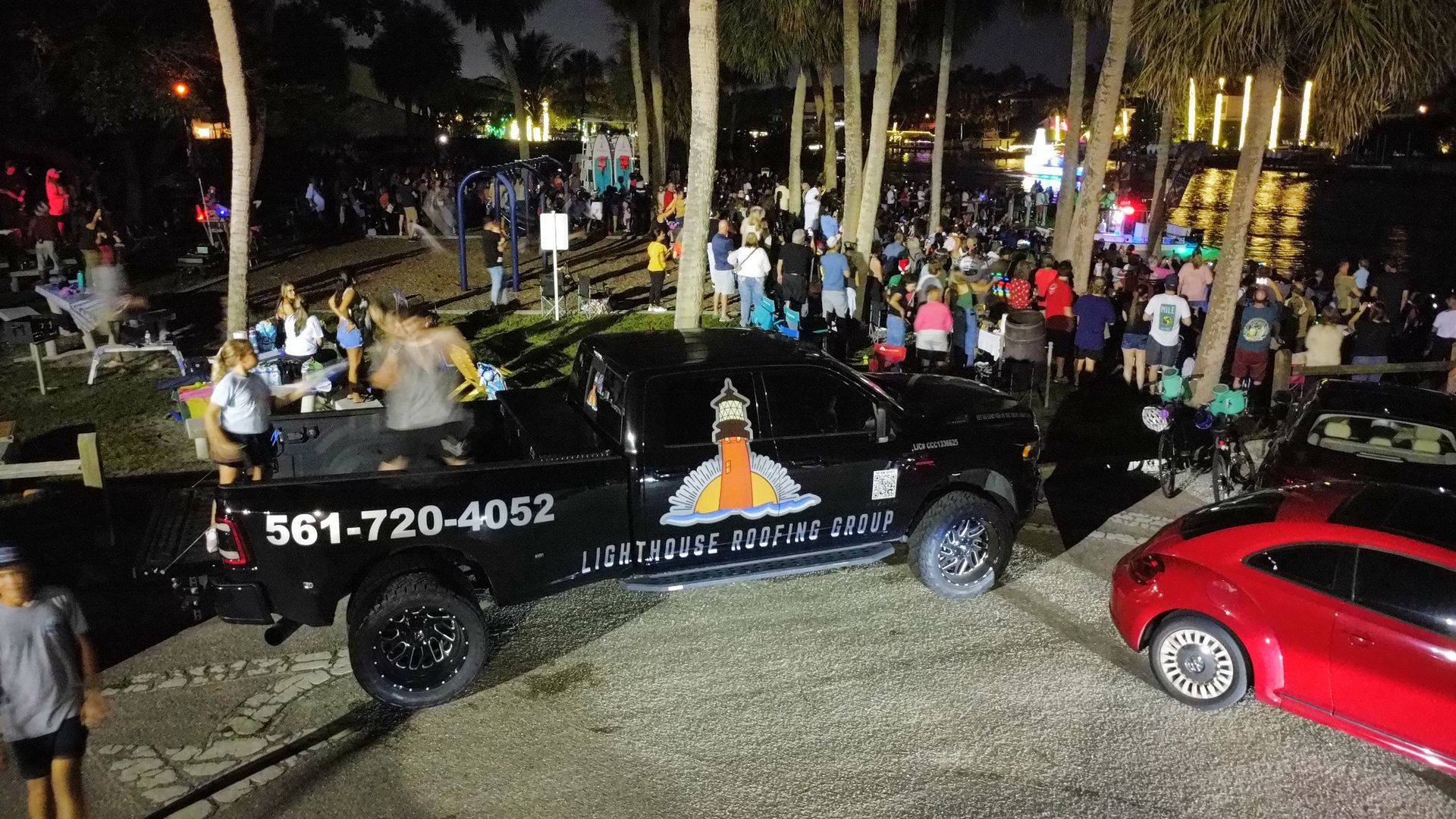 Nighttime parade float with lights, people, palm trees, and a red car beside it
