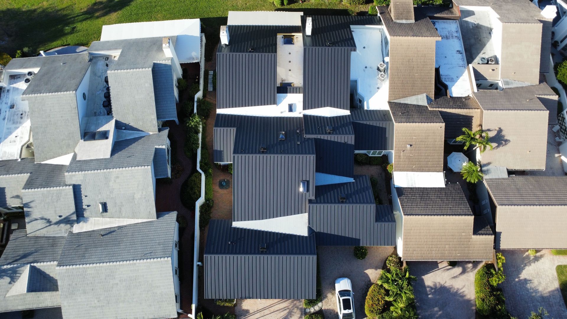 Aerial view of closely packed residential roofs, mostly gray and dark metal, with a narrow alley between houses.