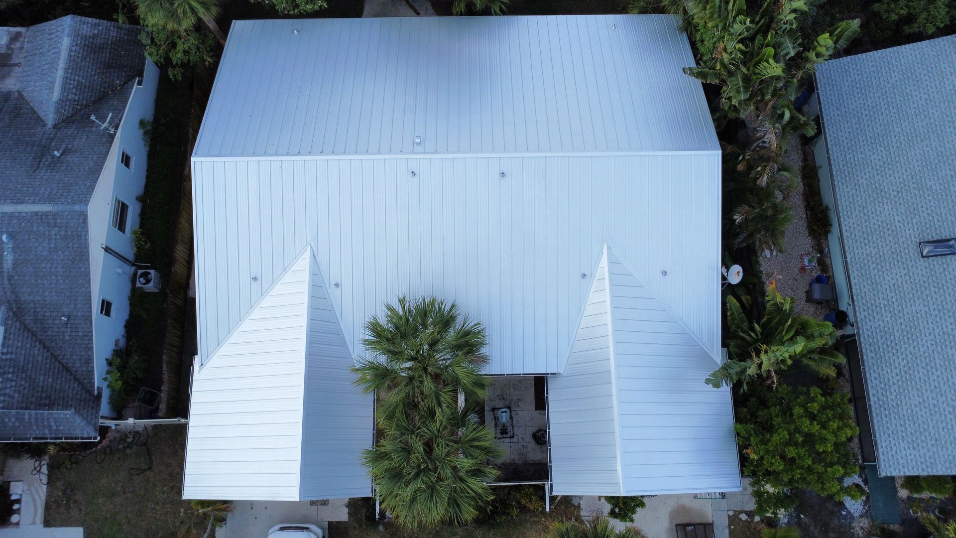 Aerial view of a white-roofed house surrounded by trees and neighboring homes.