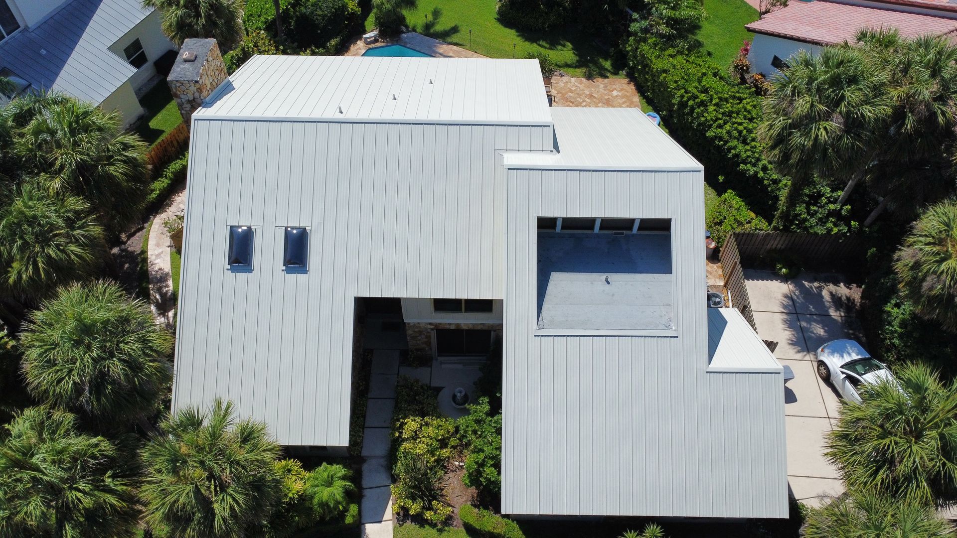 Aerial view of a white-roofed house surrounded by lush green trees and landscaping.